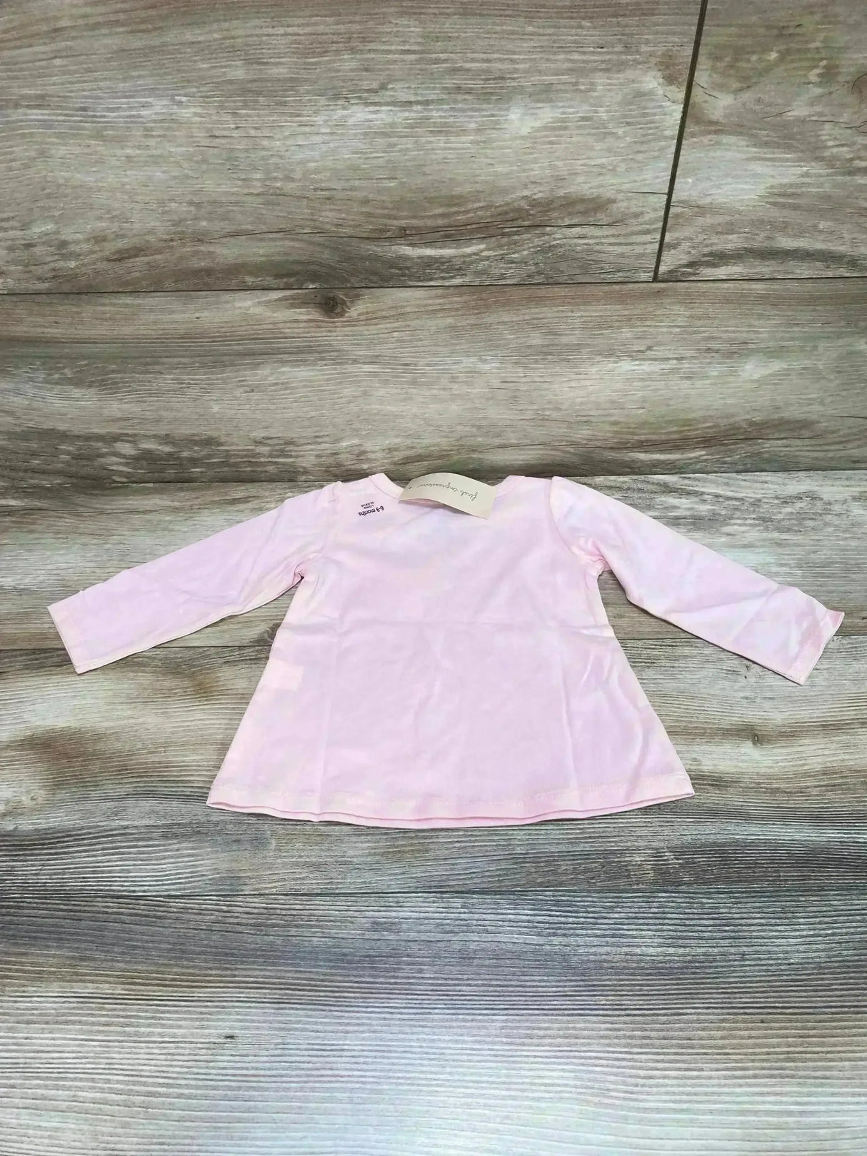 Flat-lay of First Impressions pink long-sleeve baby tunic (6-9 months) showing A-line hem and crew neckline on wood floor background