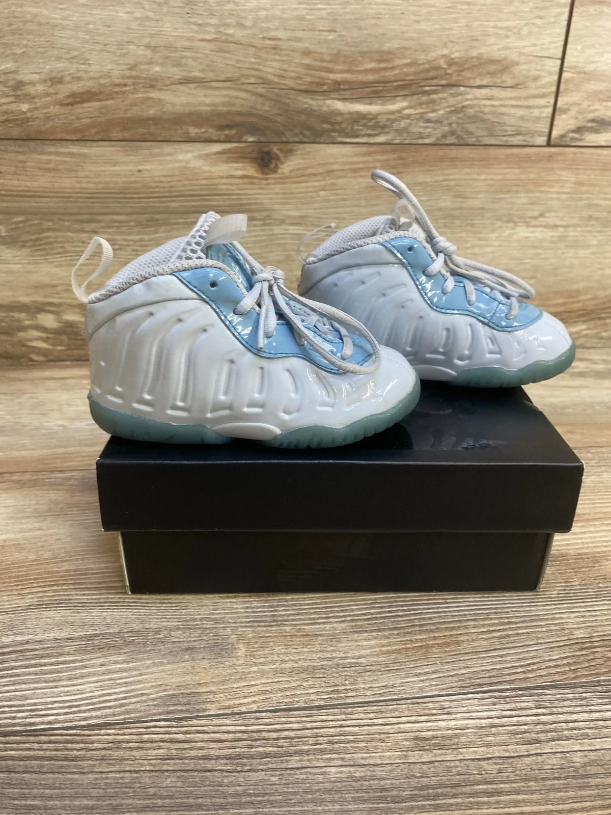 Side view of Nike Little Posite One sneakers with glossy white finish, light blue trim and translucent green sole on black box