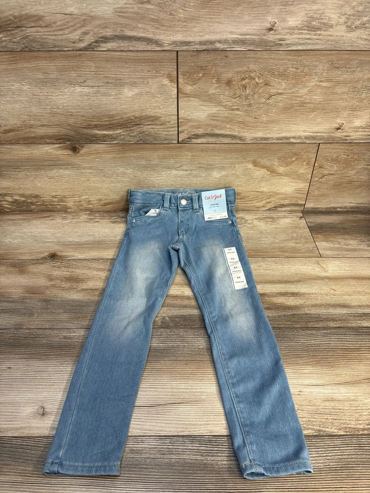Light blue kids' jeans with tags on wooden background, gently used children's clothing