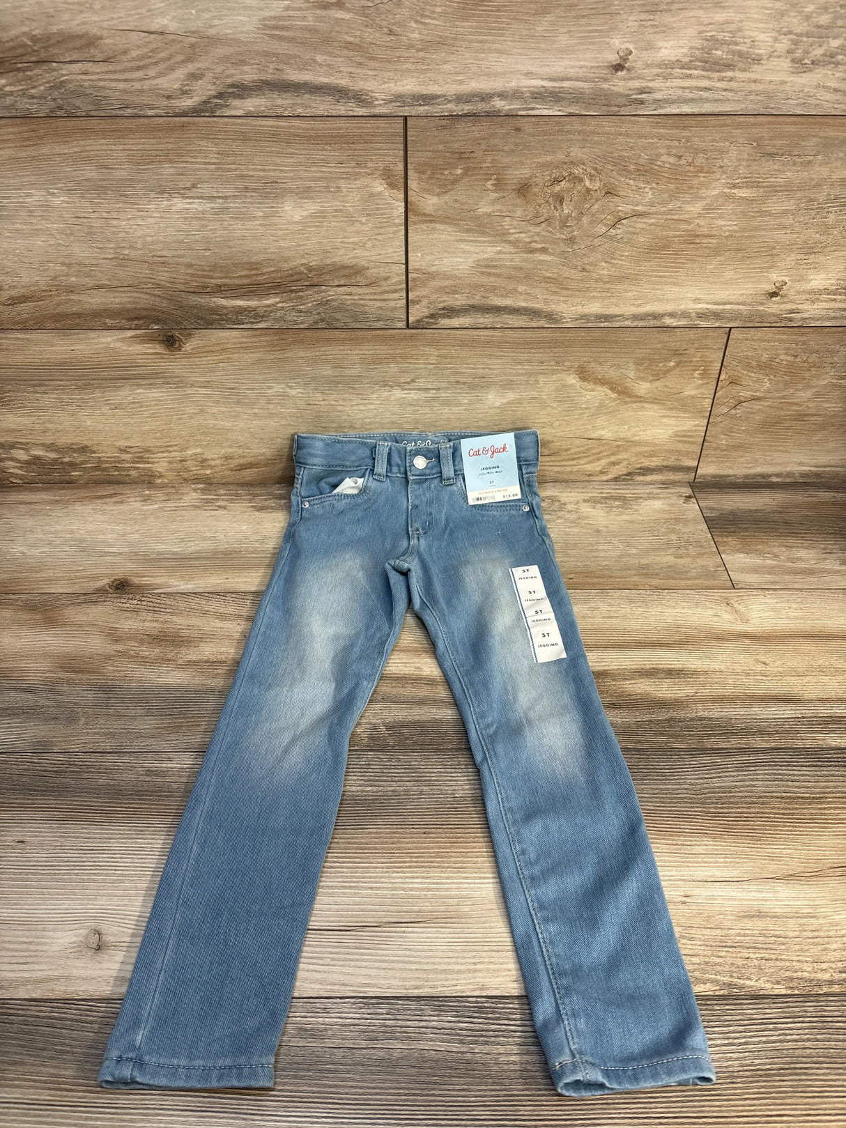 Light blue kids' jeans with tags on wooden background, gently used children's clothing