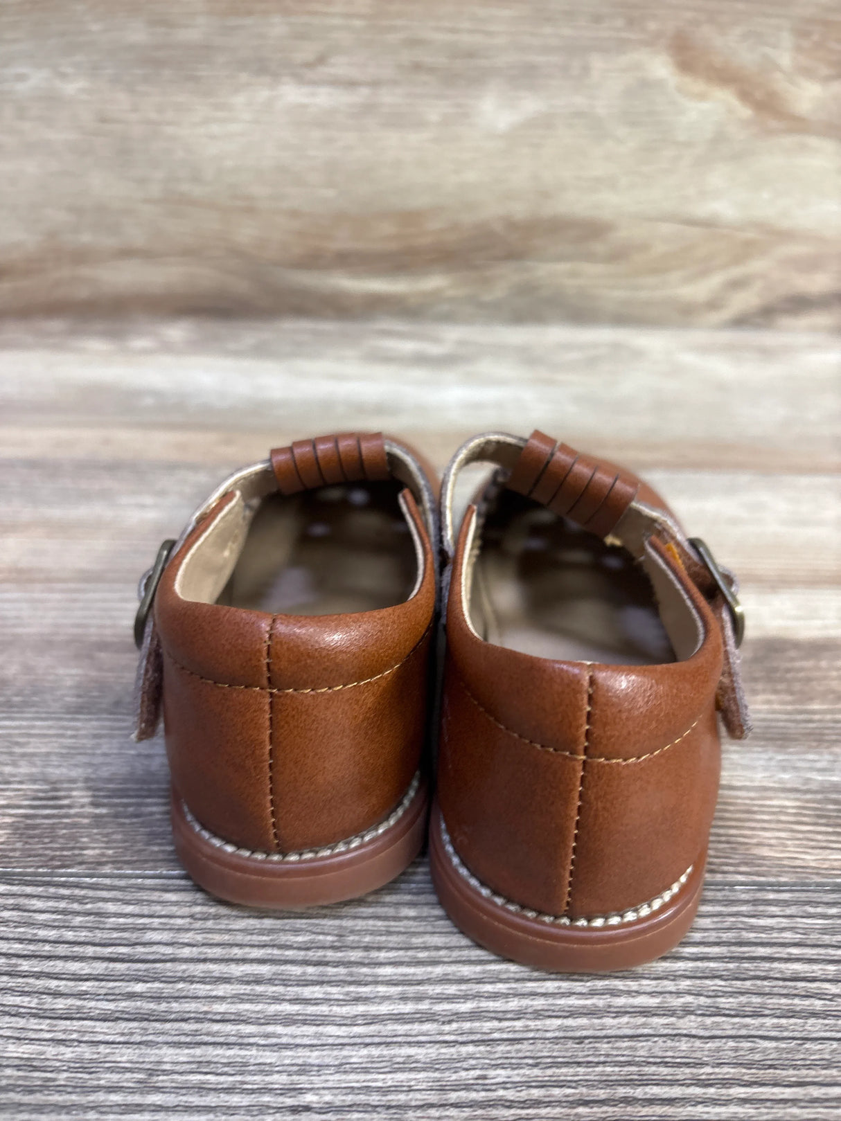 Rear view of Momo T-strap Mary Jane toddler shoes showcasing stitched back seam, buckle T-strap, and heel on wood background