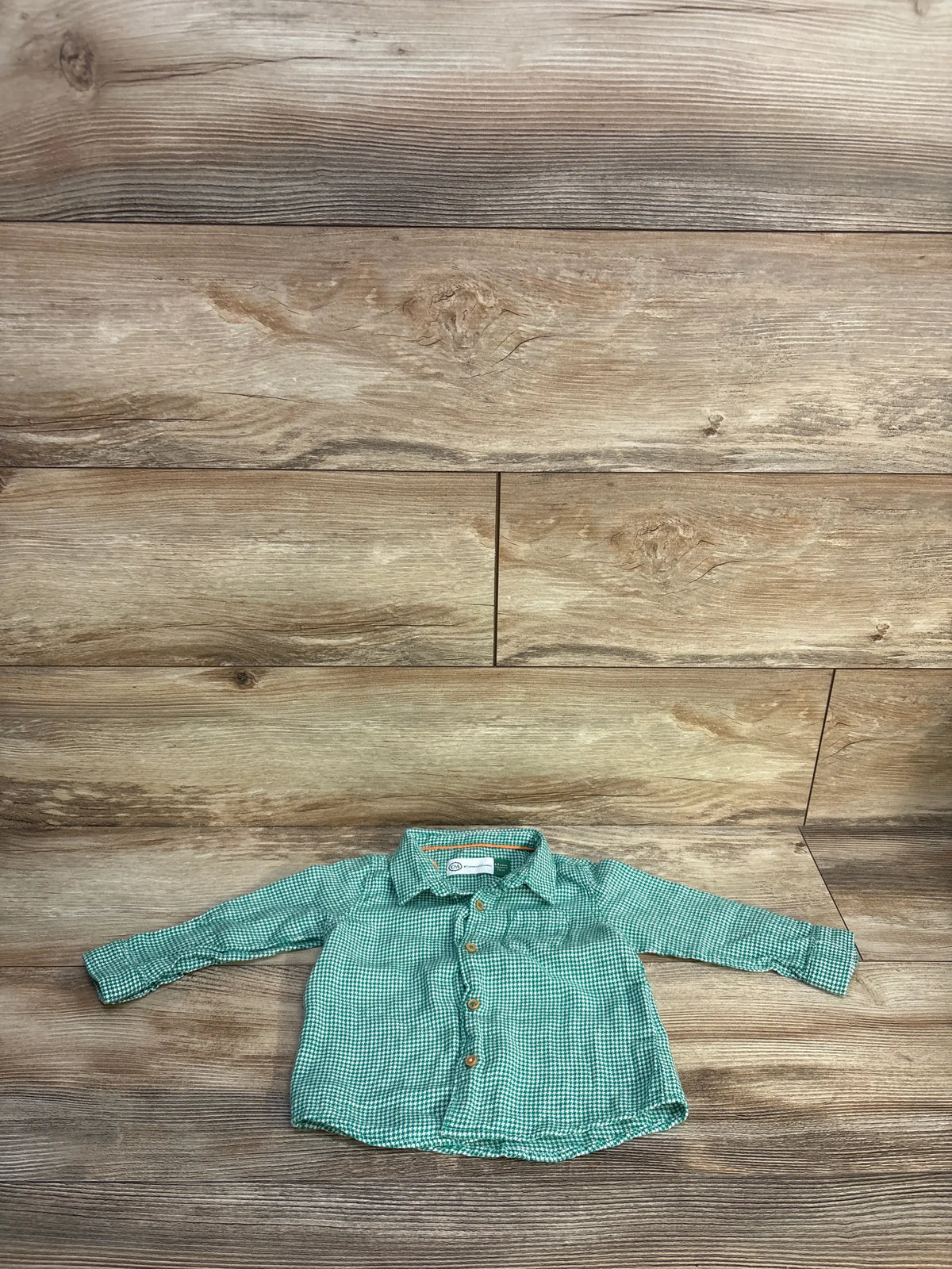 Front view of C&A green button-up shirt showcasing long sleeves, collar, and button front on a wood background