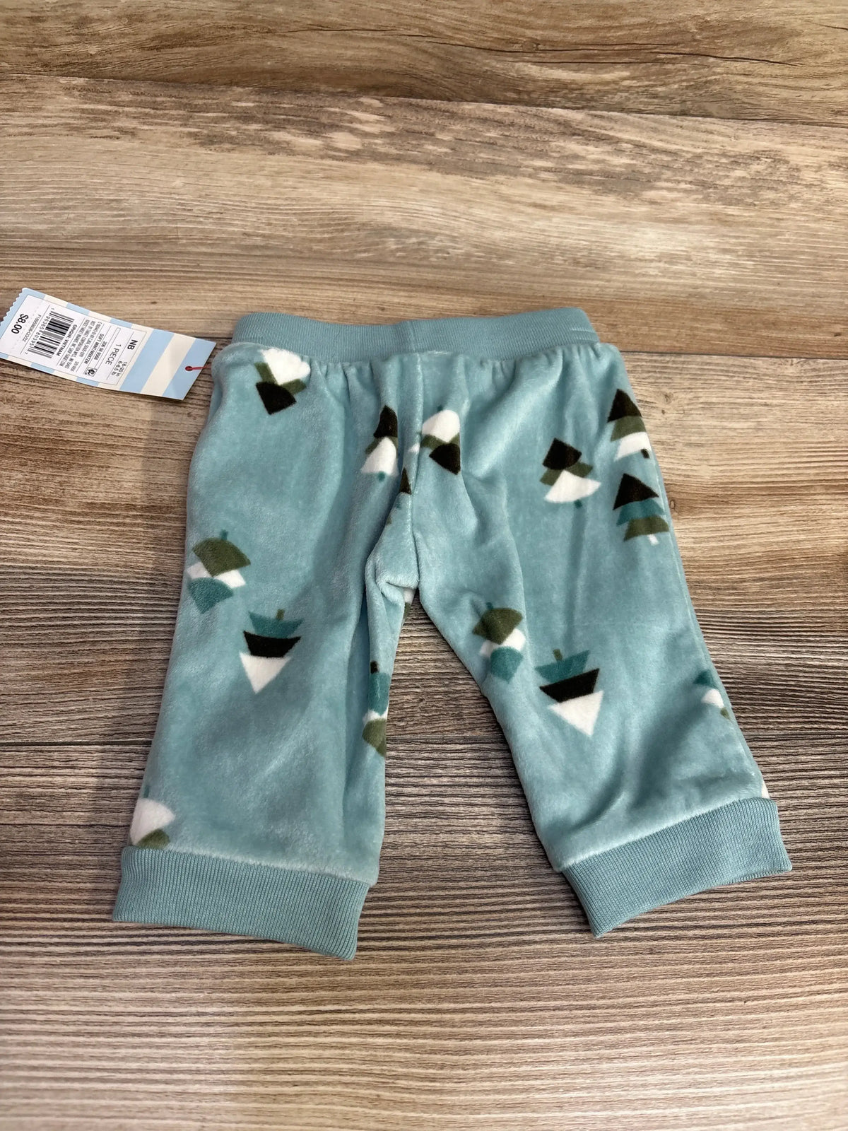 Top-down view of teal newborn velour pull-on baby pants with tree-print, elastic waist and ribbed cuffs on wood background