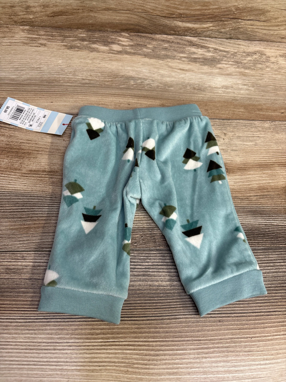 Soft blue baby pants with geometric tree print, toddler clothing on wood background