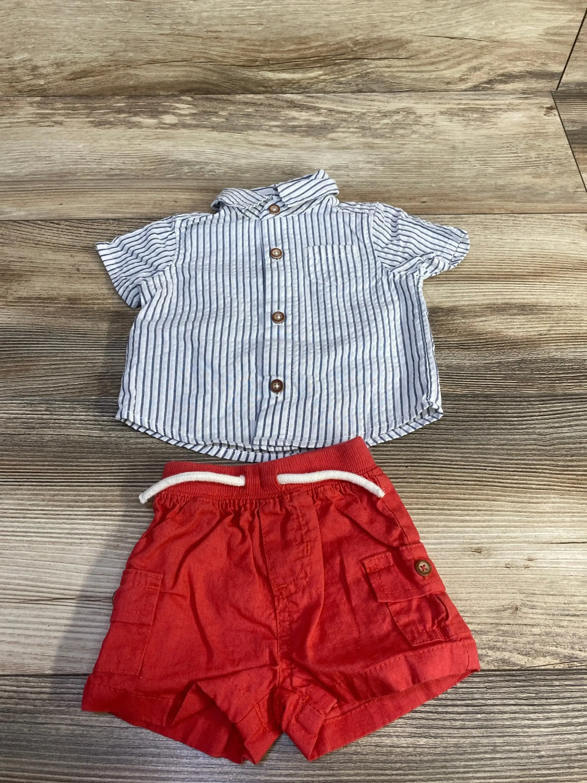 Top-down of newborn 2-piece set: white striped button-up shirt and red drawstring shorts on wood background