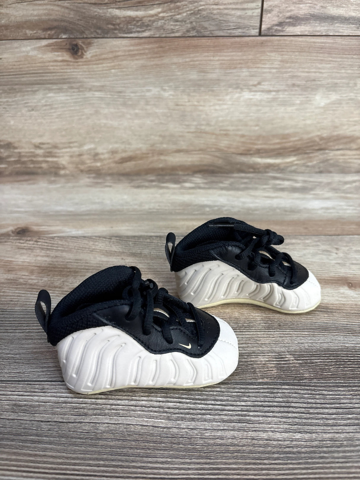 Black and white baby sneakers on wooden floor, Nike toddler foamposite shoes