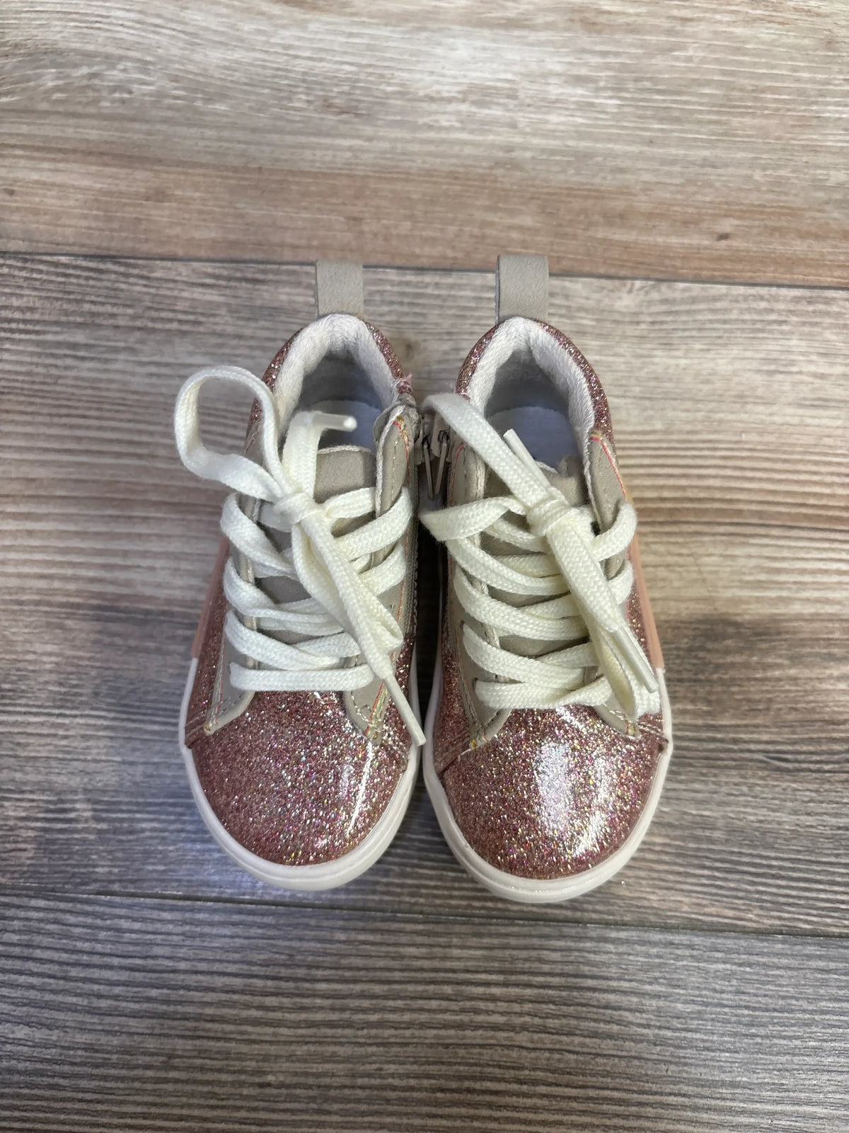 Top view of Zara pink glittery high top sneakers showcasing white laces, side zippers and pull tabs on a wood grain background