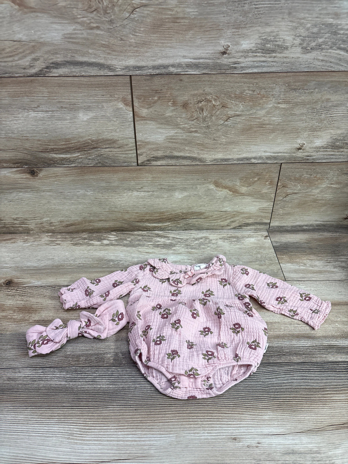 Flat lay of Rabbit and Bear organic two-piece gauze romper and headband set with pink floral print on a wood plank background