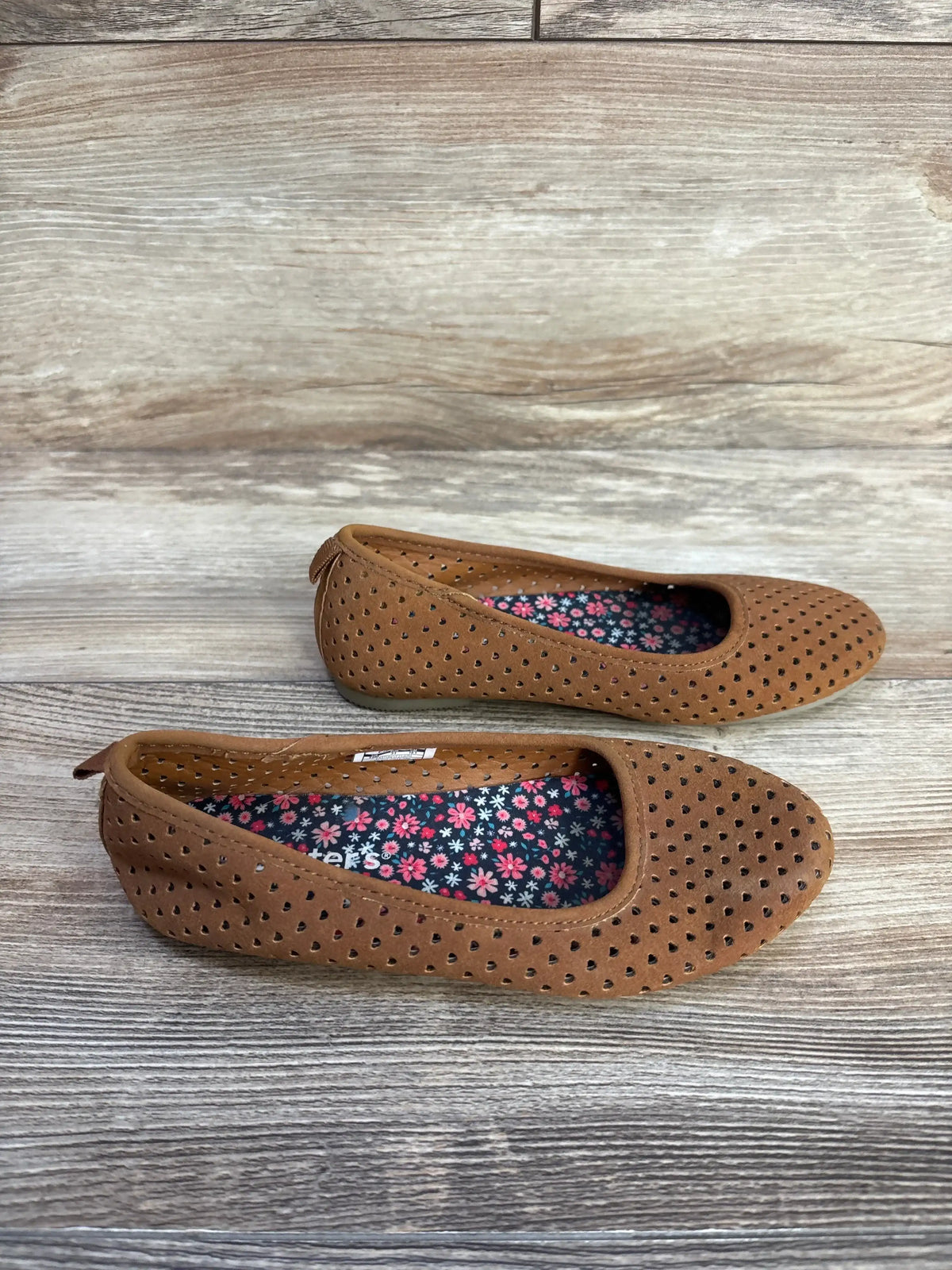 Top-down view of Carter’s Easton Heart flats showing brown perforated upper and floral insoles on light wood background