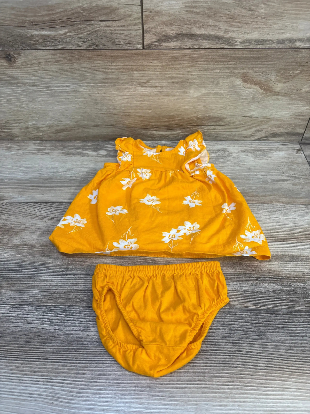 Flat lay of yellow baby dress and bloomers showing white floral print and ruffled sleeves on wood background