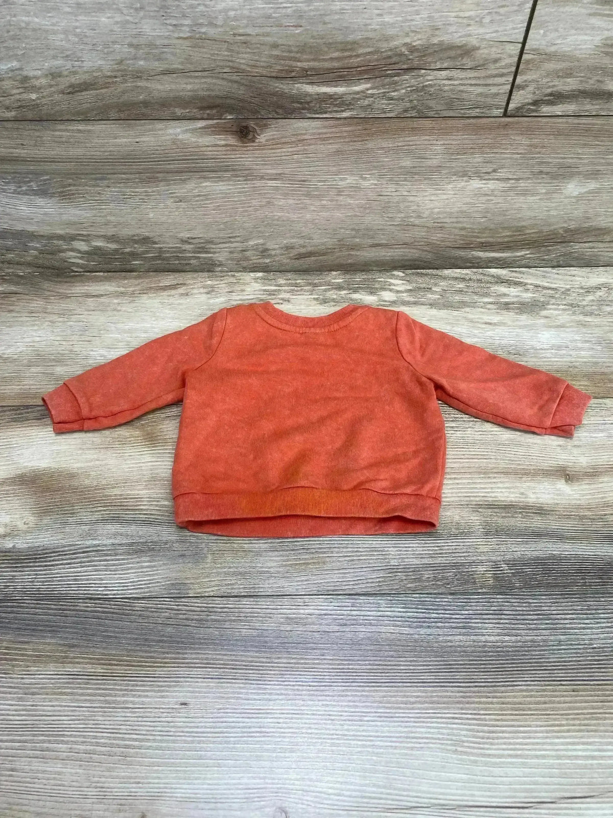 Back of Cat & Jack Oh So Lovable sweatshirt, orange, size 0-3M, showing long sleeves and ribbed hem on wood background