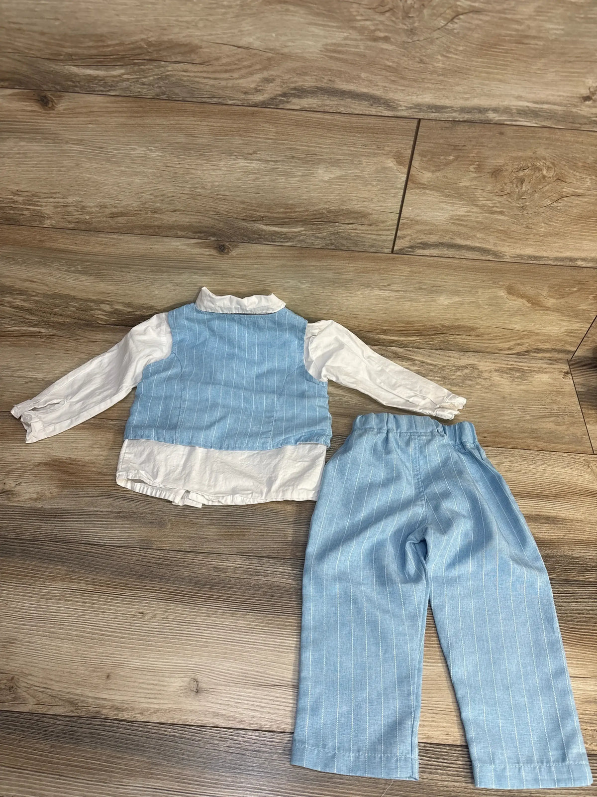 Baby boy’s light blue pinstripe vest set with white long-sleeve shirt and matching pants, laid on wood floor