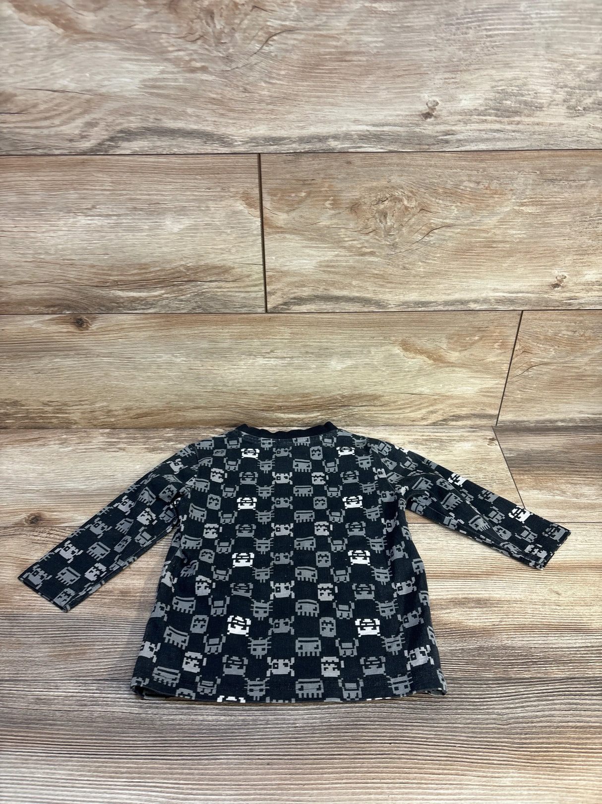 Long sleeve kids shirt with gray pixel monster pattern, laid flat on wood floor.