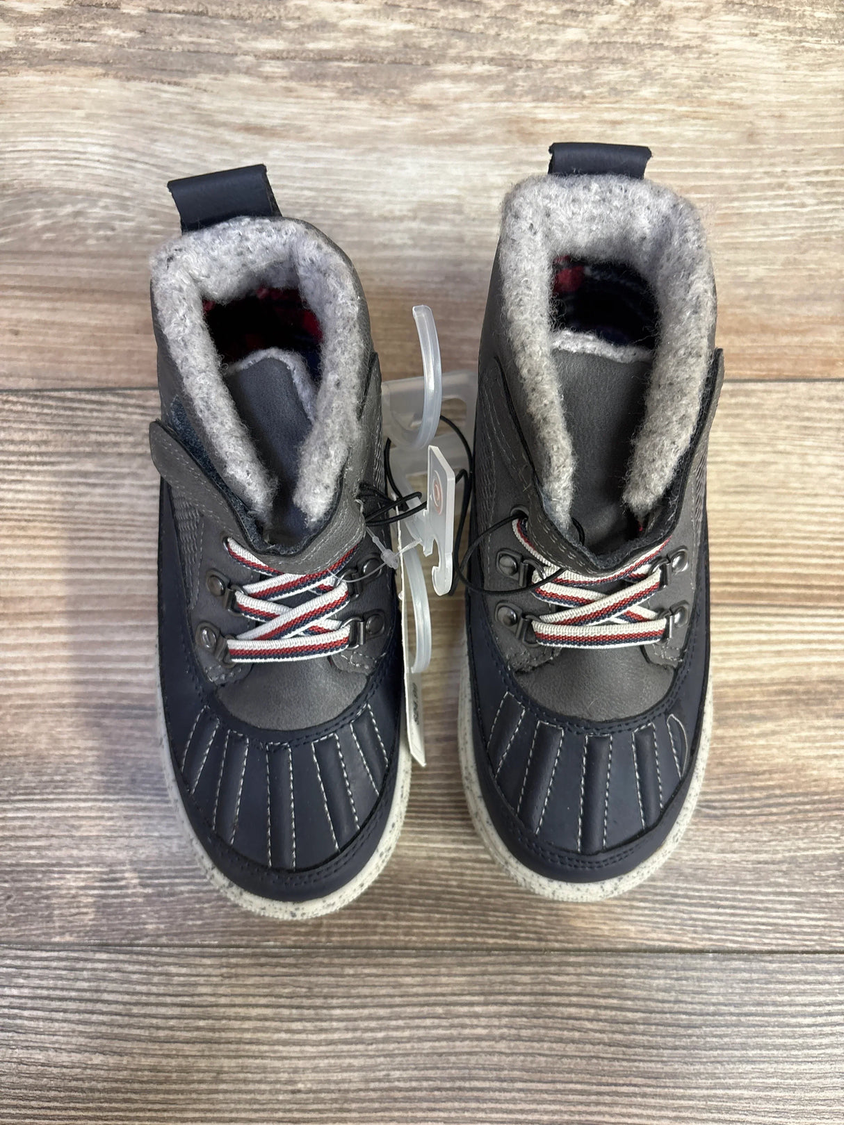 Pair of black winter boots with gray wool lining and red-white striped laces on wooden floor