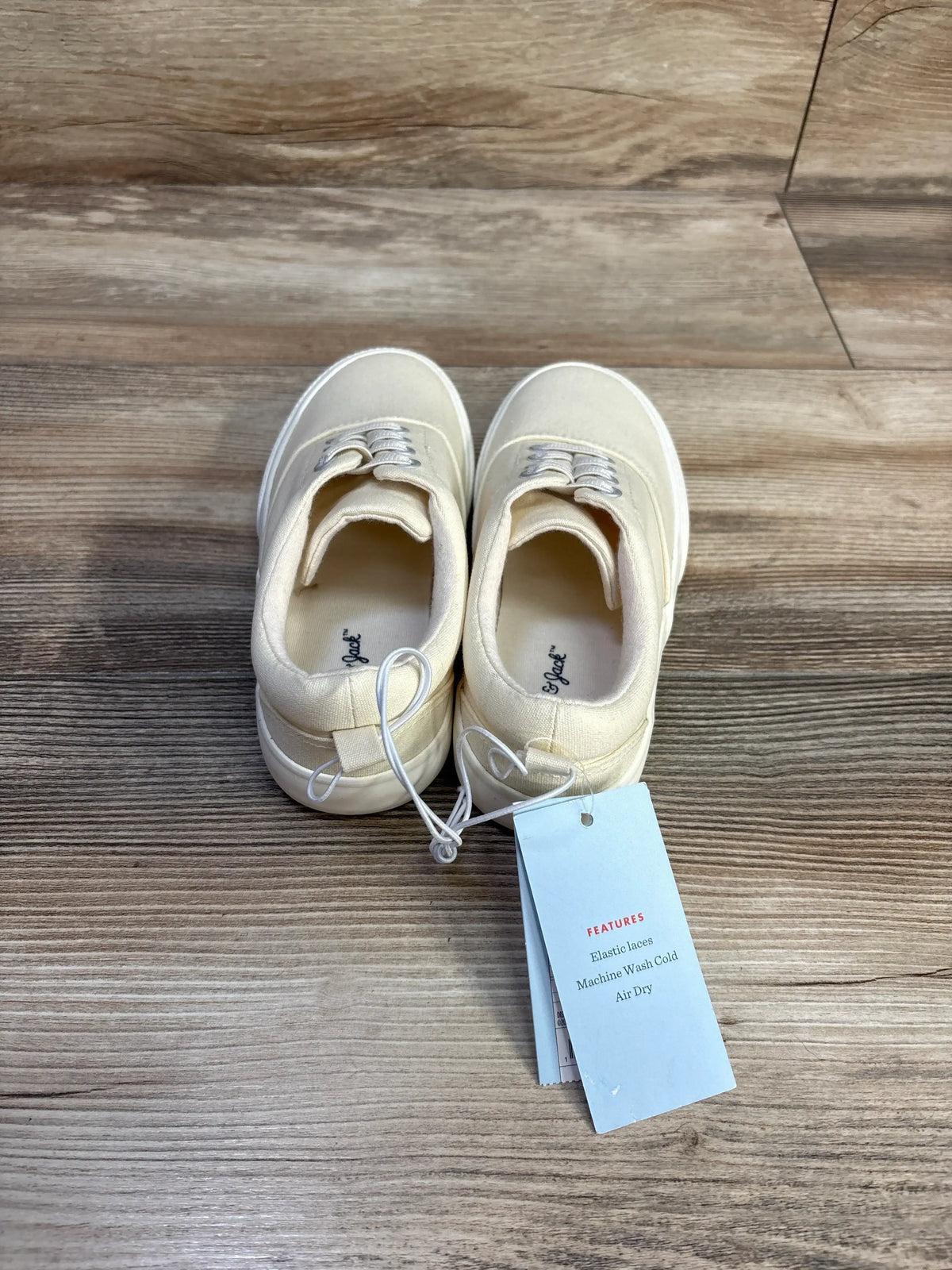 Back view of Cat and Jack Tyler slip on sneakers in off white showcasing elastic laces and hangtag on wood plank floor