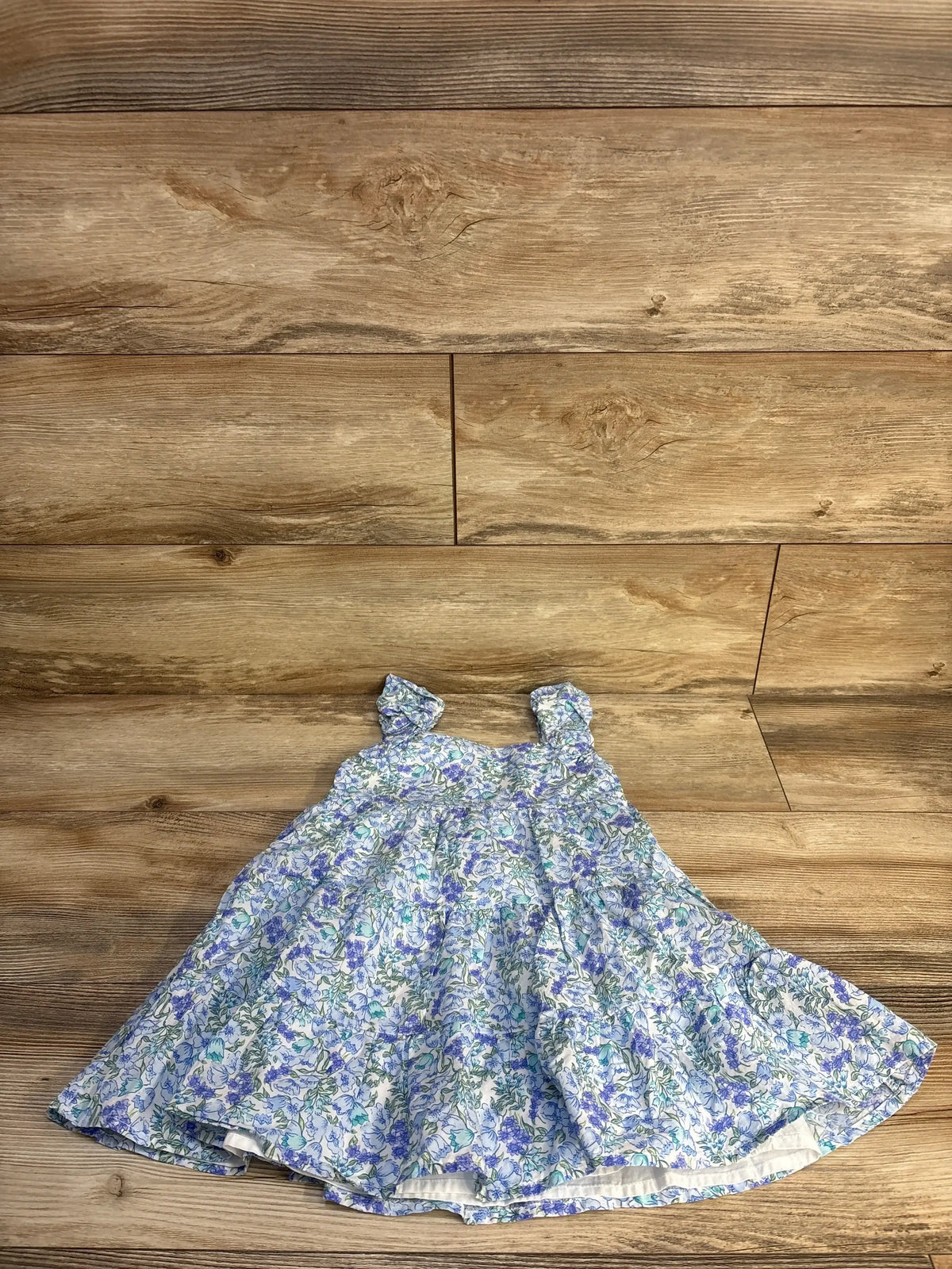 Flat lay of toddler blue ditsy floral tiered dress size 3T showing ruffled straps and gathered bodice on wooden floor