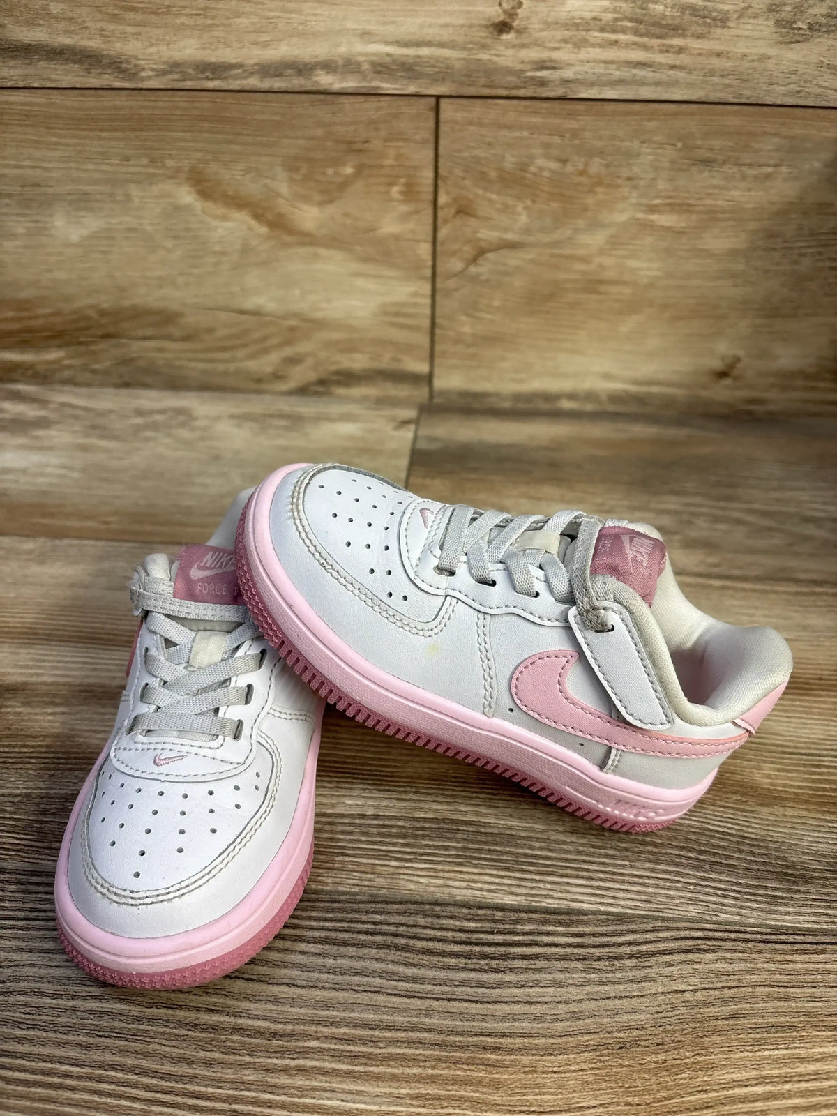 Front-right view of Nike Air Force 1 EasyOn toddler sneaker, white with pink accents, pink Swoosh and Velcro on wood floor