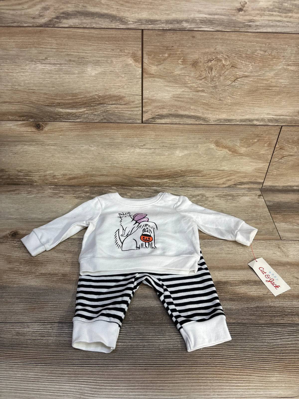 Flat lay of Cat and Jack Halloween set showing white sweatshirt, striped joggers and festive graphic on wood floor