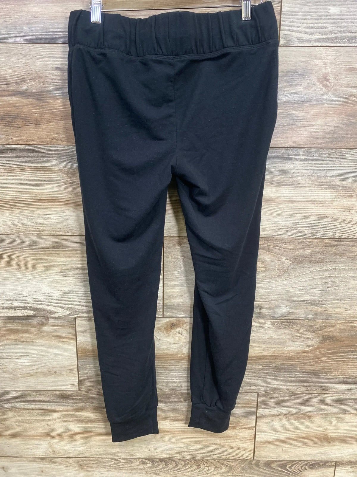 Back view of Isabel maternity drawstring joggers in black showing elastic waistband and cuffed tapered legs against wood planks