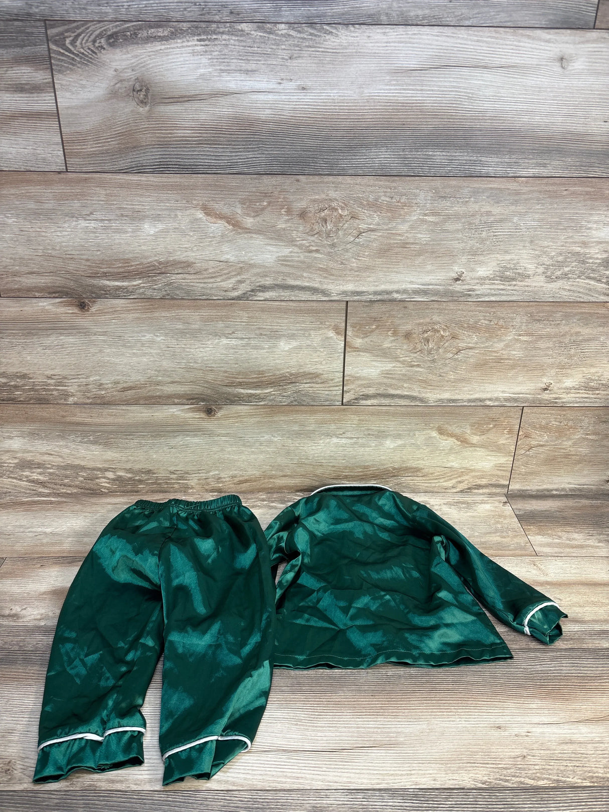 Emerald green satin pajama set with white trim, laid on wood floor