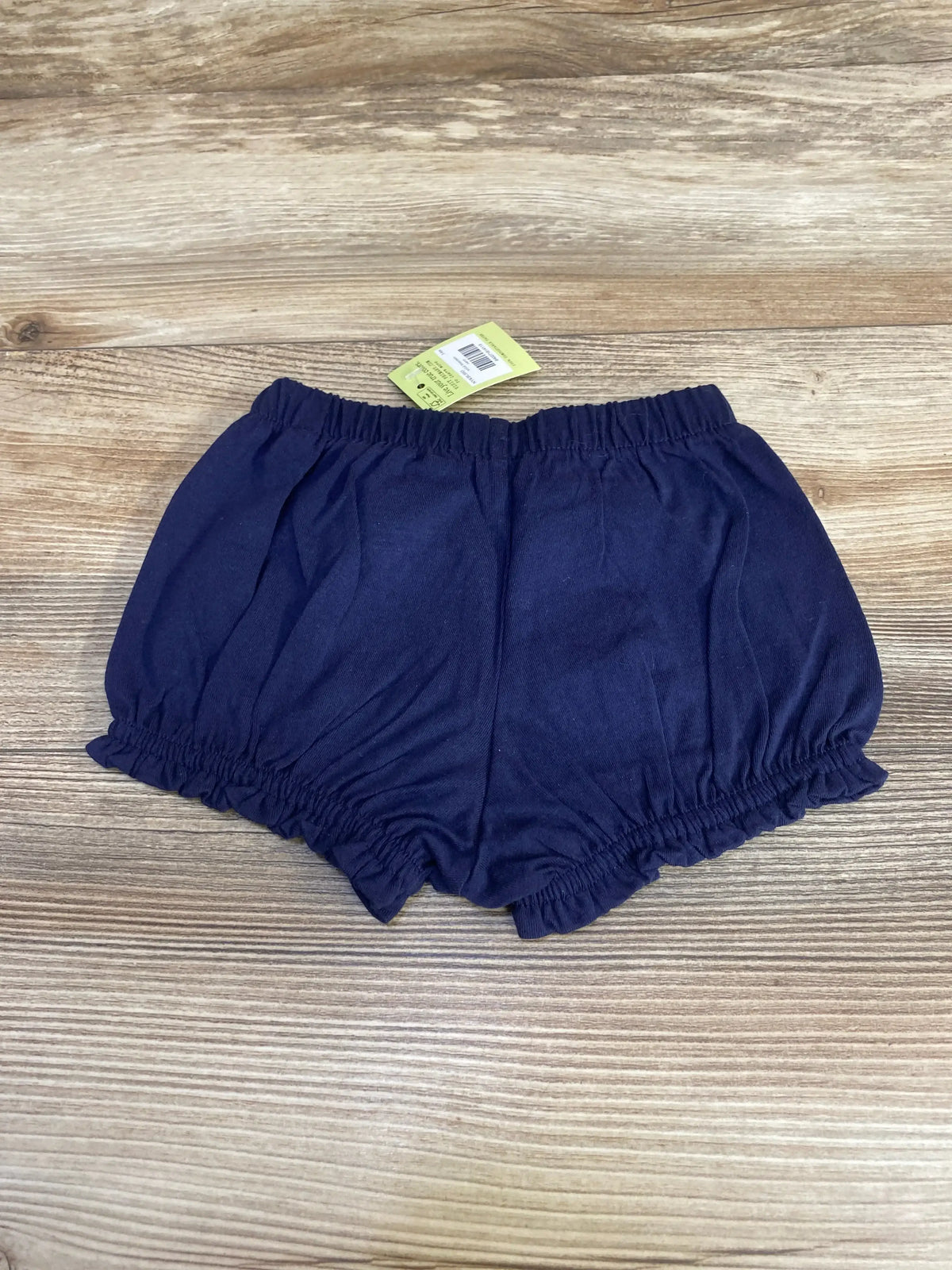 Top-down view of navy baby bloomer size 3-6m showing elastic waistband and ruffled leg openings on wood background