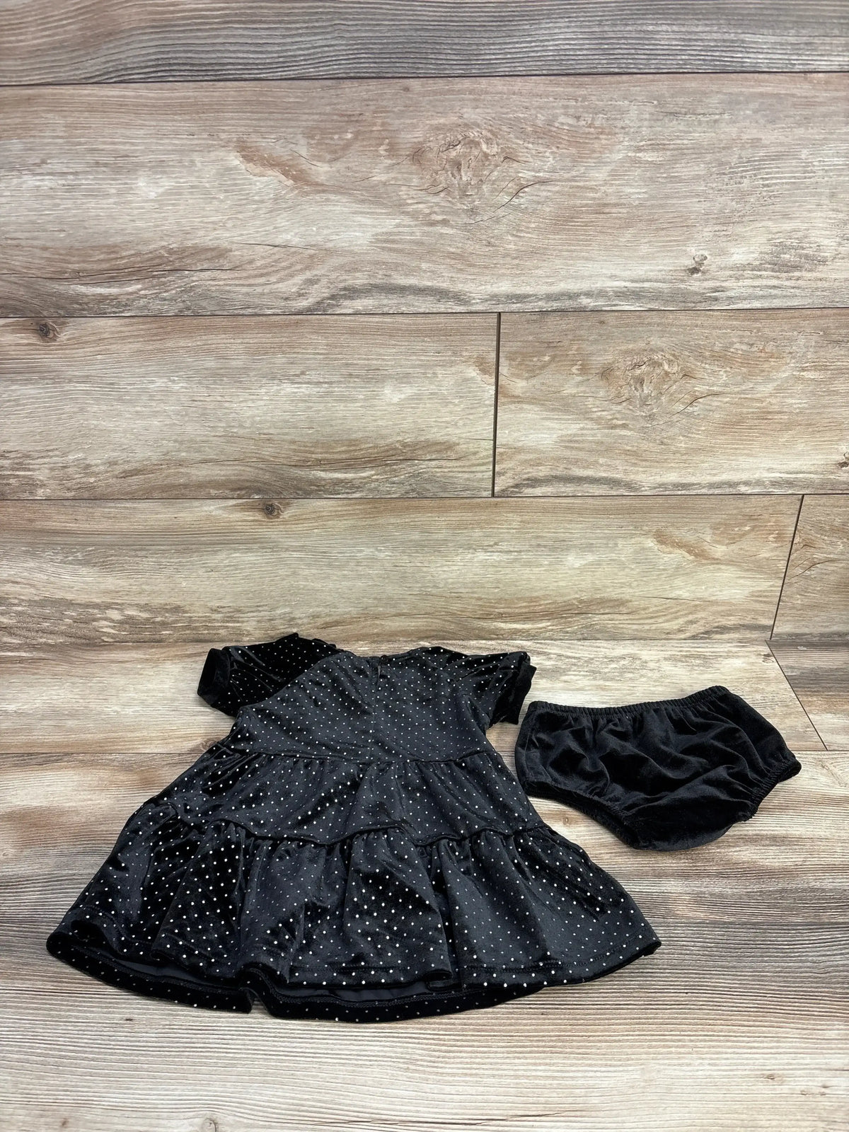Flat lay of Habitual Kid black velvet metallic polka dot dress and matching bloomers tiered skirt on wood floor