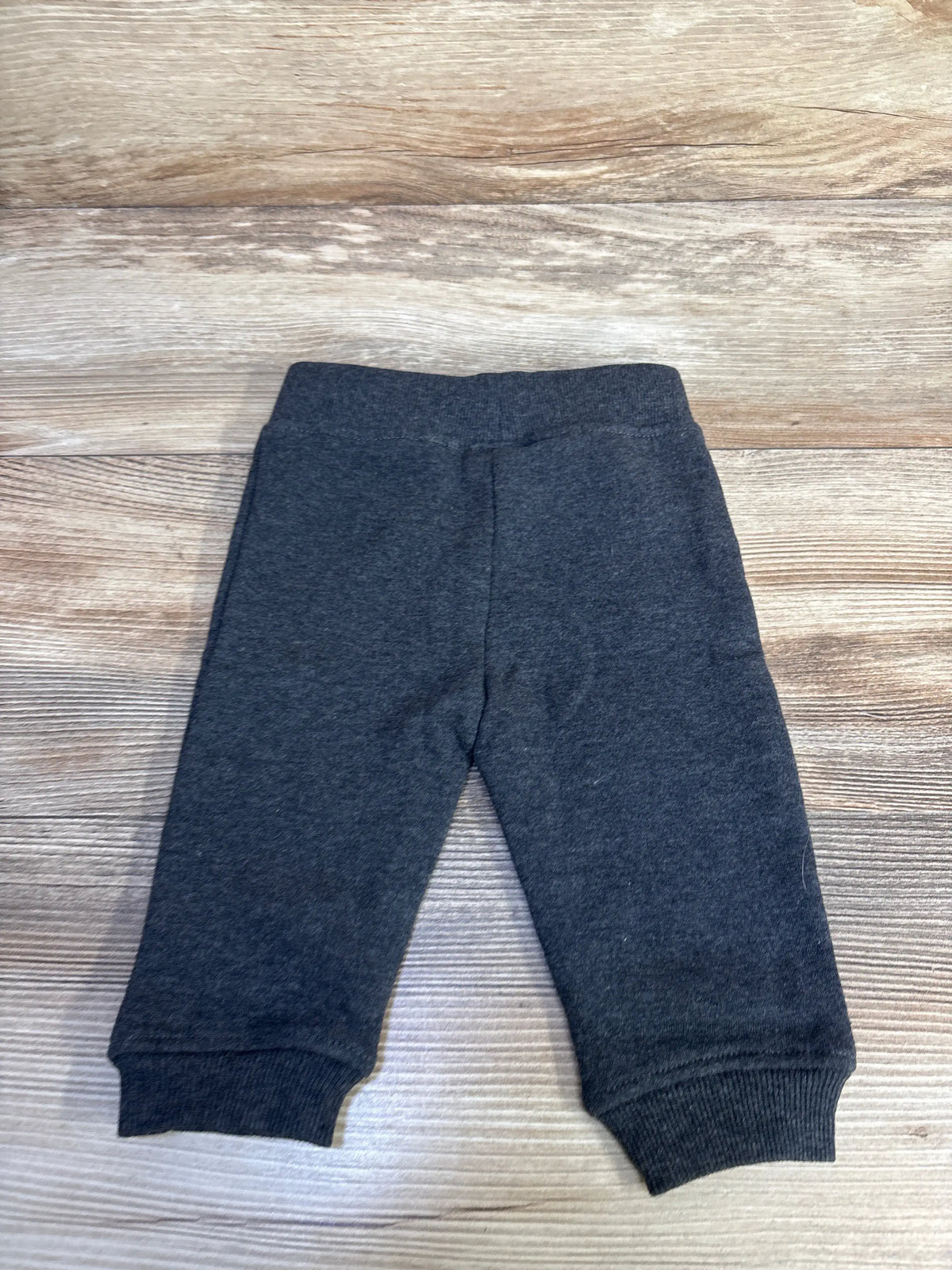 Front view of grey joggers, size 3 to 6 months, showcasing elastic waistband and cuffed ankles on a wood surface