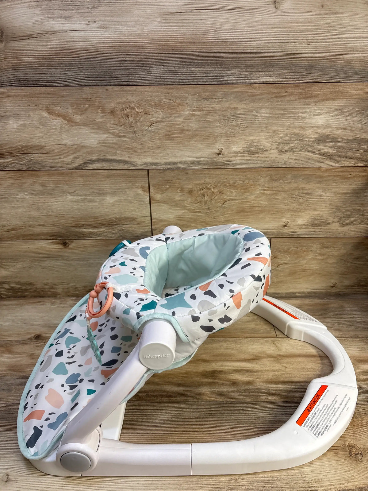 Angled view of Fisher Price Sit-Me-Up Floor Seat in Pacific Pebble with patterned padded seat and wide base on wood floor