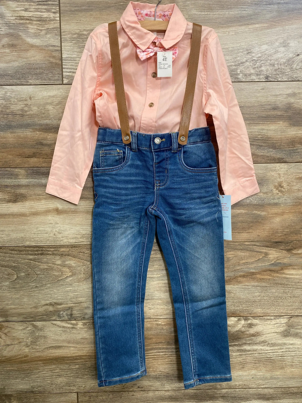 Front view of toddler 4-piece suspender set with pink collared shirt, floral bow tie, blue jeans and brown suspenders on wood