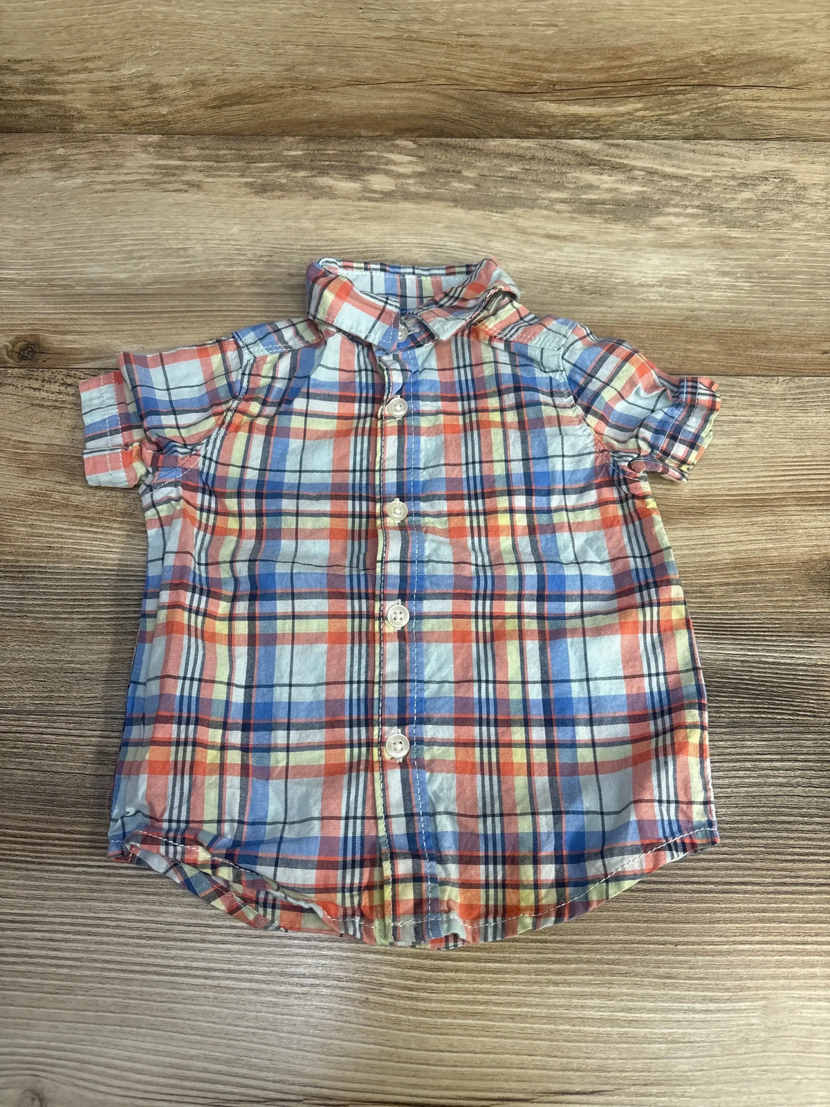 Top-down view of blue and orange plaid baby button-up shirt 3-6m with rolled sleeves and front buttons on wood background