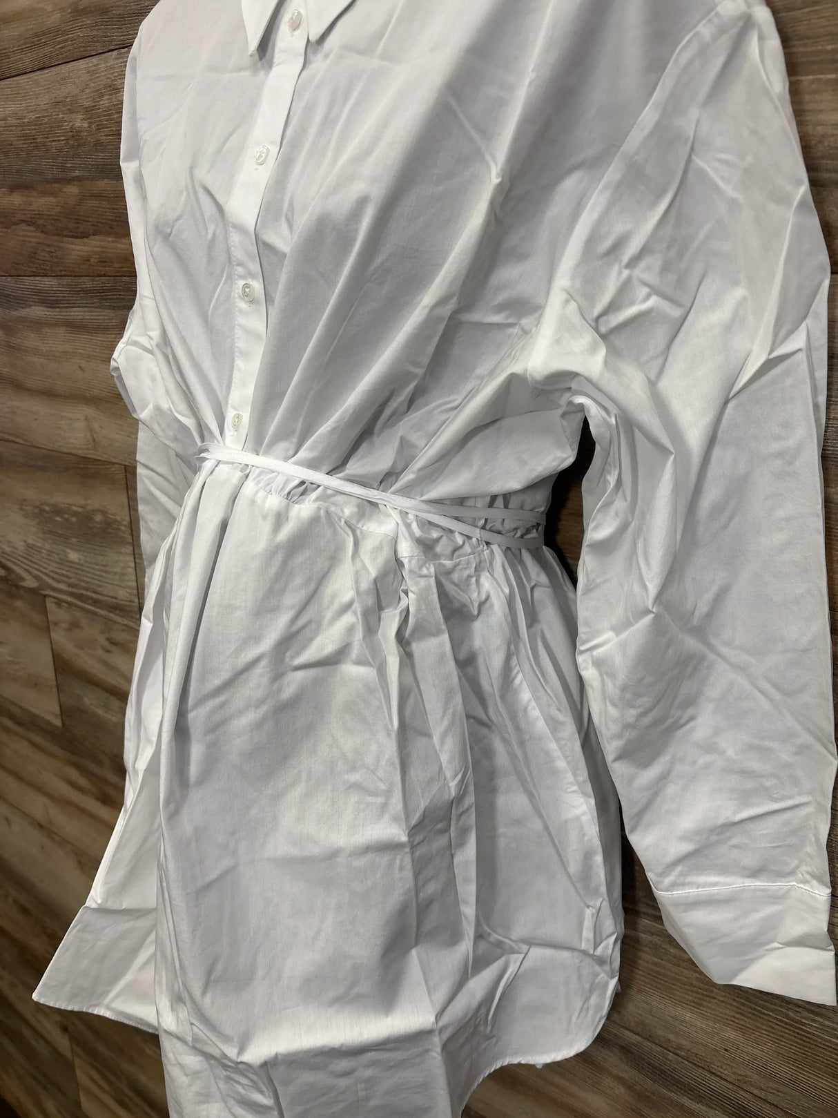 Side-front view of white maternity popover shirt on mannequin showcasing button front and tie waist against wood plank background