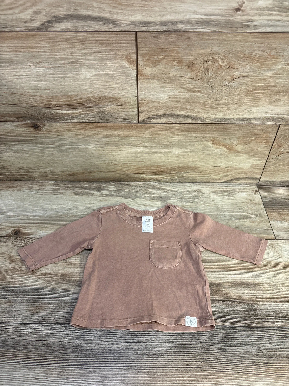 Front view of Cotton On brown baby long sleeve shirt, size 0-3 months, with chest pocket on wood-grain background