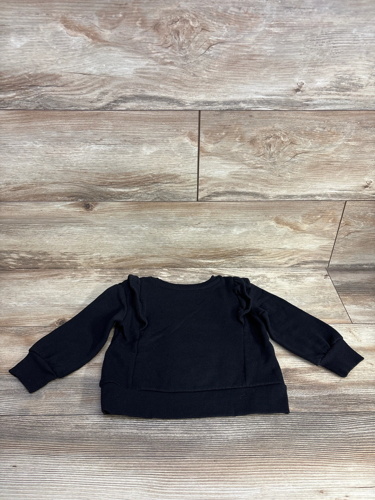 Black toddler sweater with ruffled shoulders on wooden floor