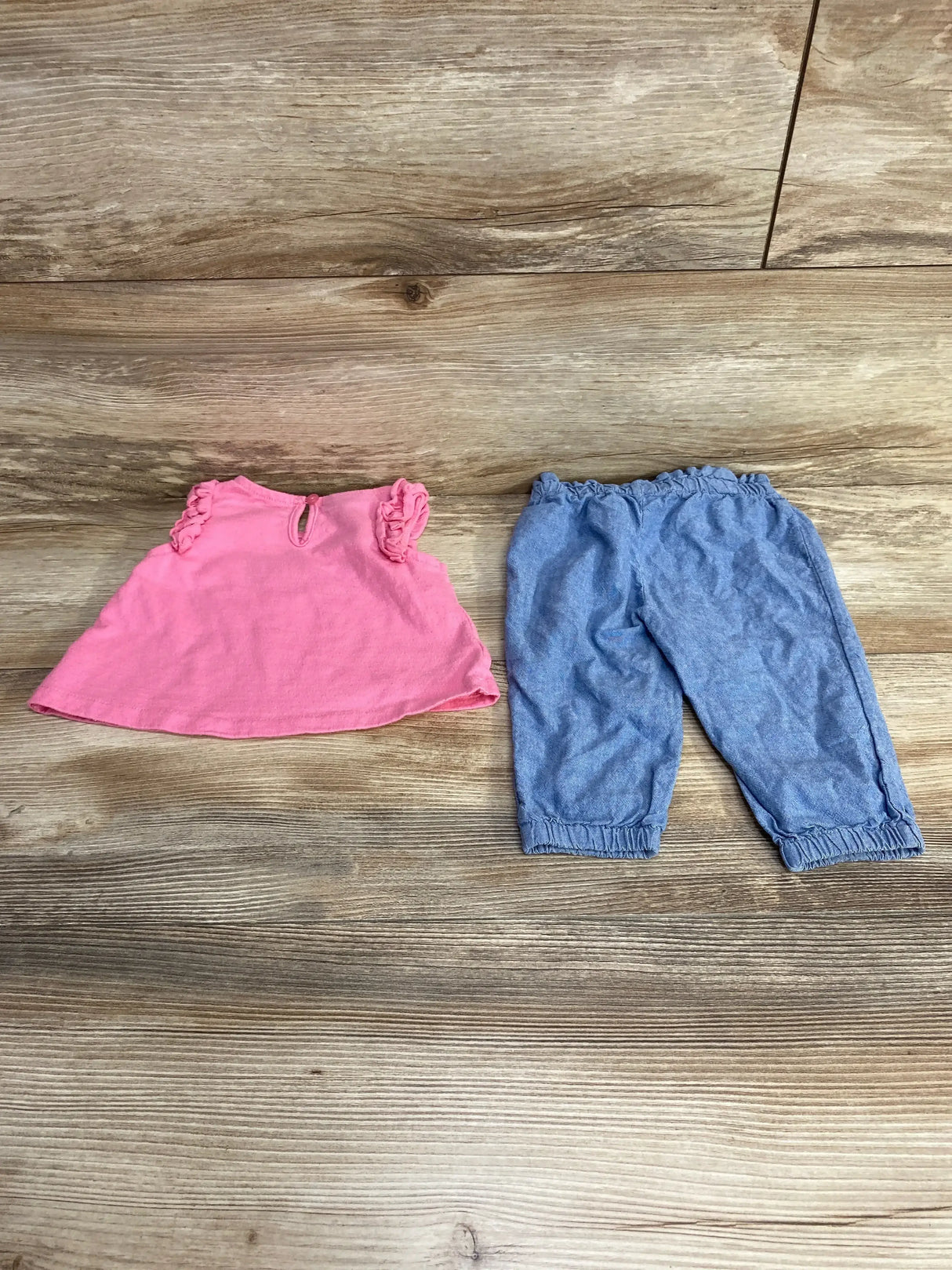 Flat lay of Tommy Hilfiger 2pc set with pink top featuring flutter sleeves and blue chambray pants on wood plank floor