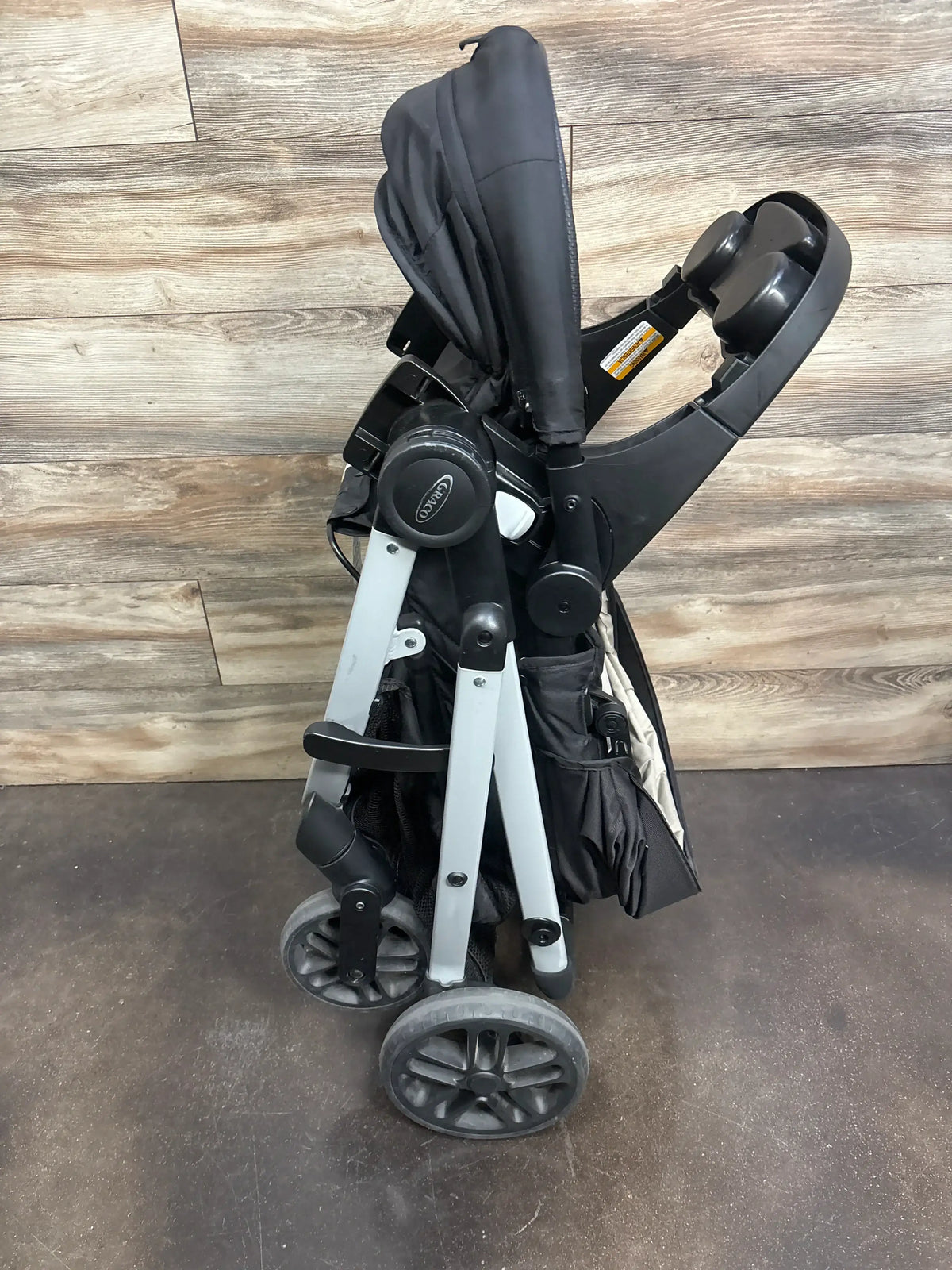 Rear view of Graco Modes Pramette stroller showcasing its folded frame, wheels, and storage basket on a wood floor