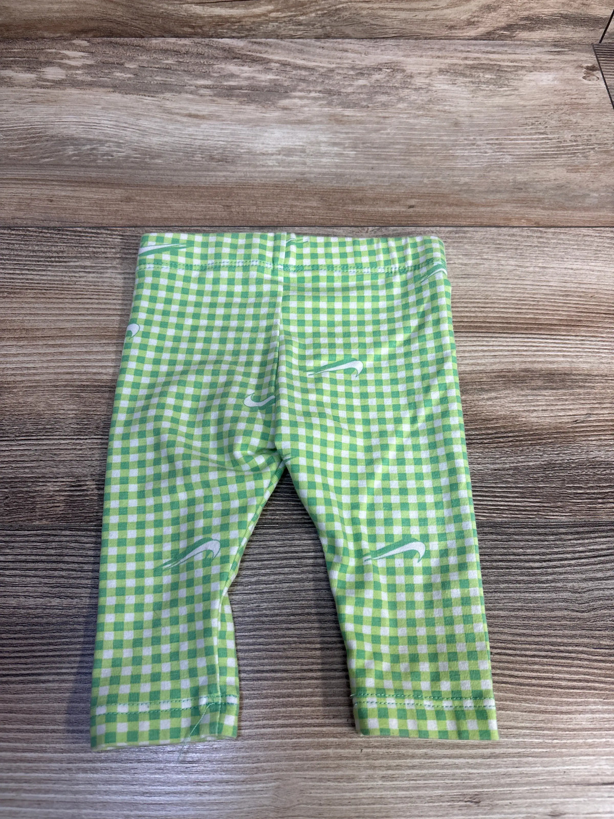 Front view of Nike green leggings showcasing a green and white check pattern and Nike swooshes with a wood background