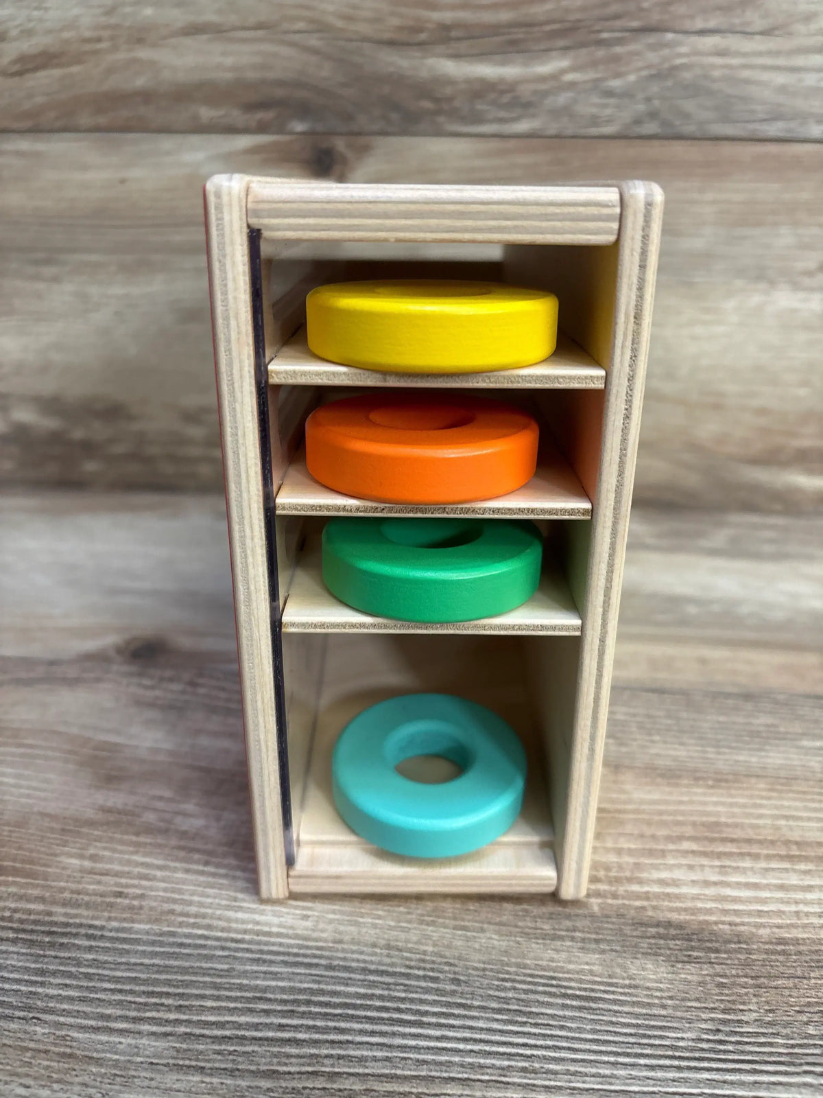 Front view of Lovevery Count and Slide Ring Chute showcasing wood tower with yellow orange green and teal stacked rings on wood plank floor
