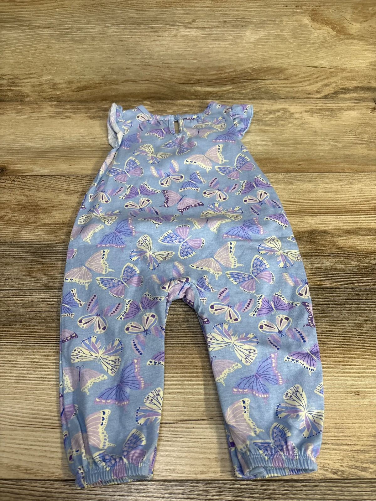 Flat lay of purple butterfly-print baby romper showing flutter sleeves and elasticized ankle cuffs on wood background