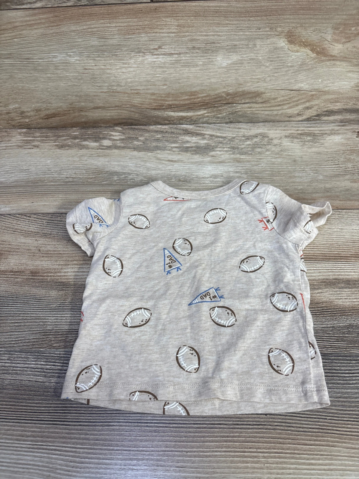 Front view of beige First Impressions baby football-print shirt showcasing short ruffle sleeves and all-over football and pennant print on wood background