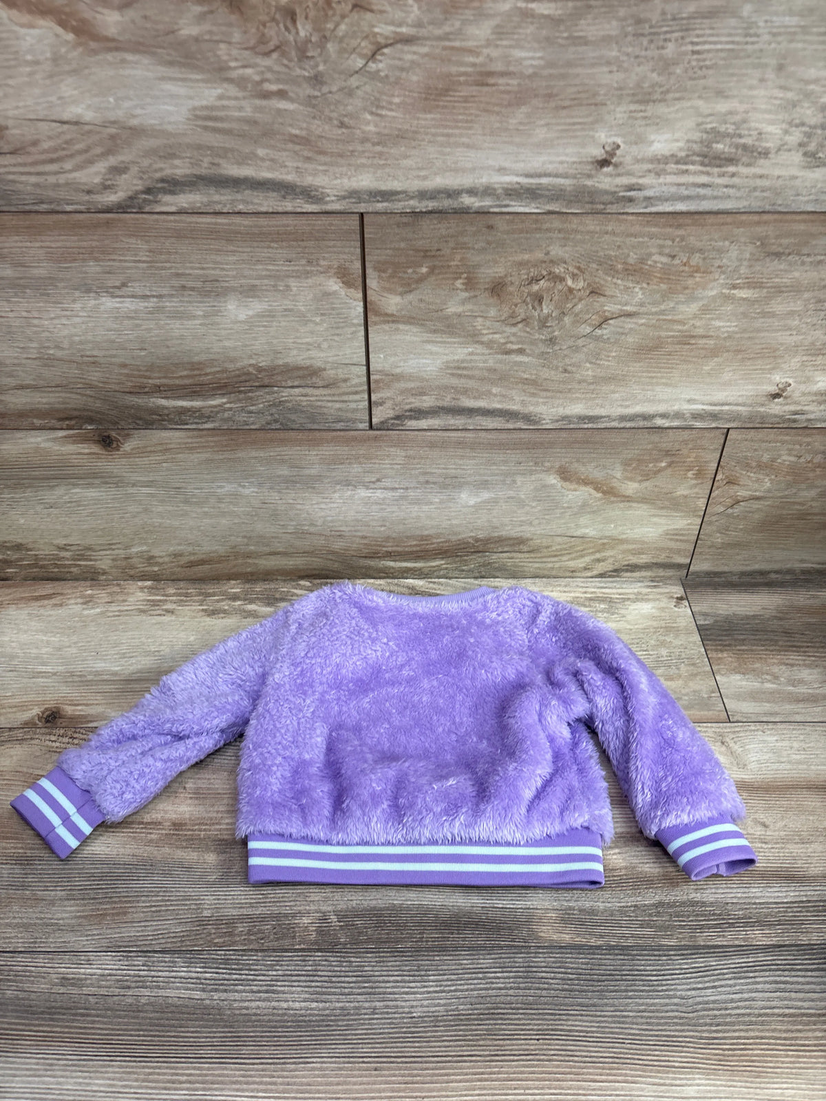 Purple plush baby sweatshirt with white striped cuffs and waistband on a wood background.