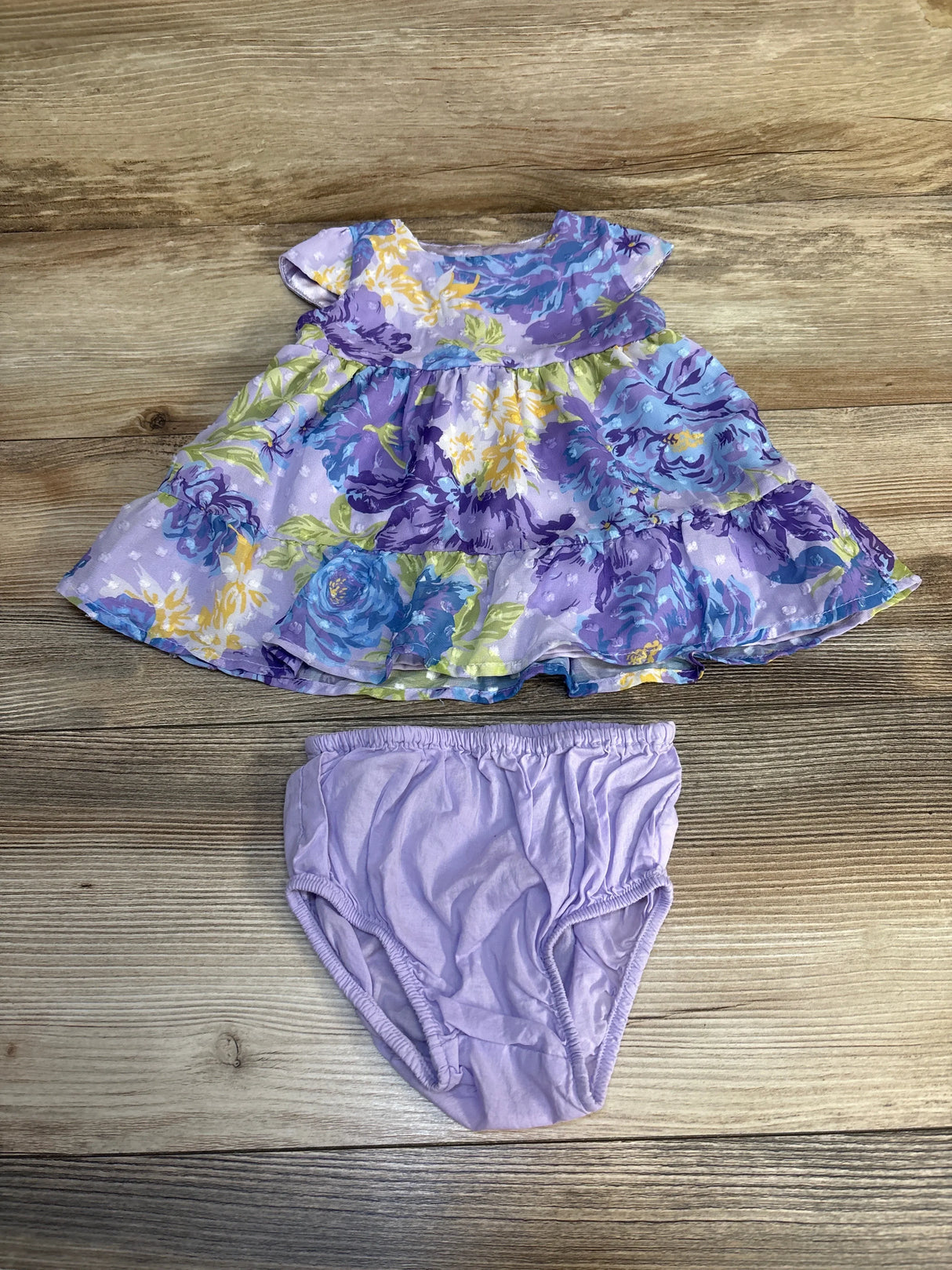 Purple floral baby dress with matching lavender bloomers on wood background