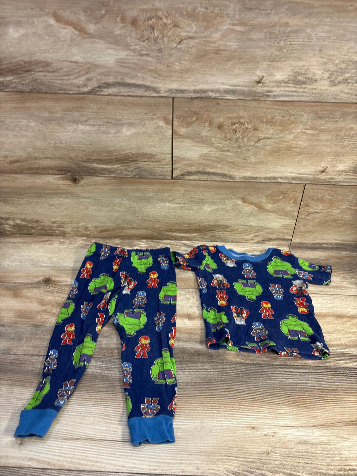 Flat lay of Marvel Avengers toddler 2 piece pajamas showing blue top and pants with Avengers character prints on wood background
