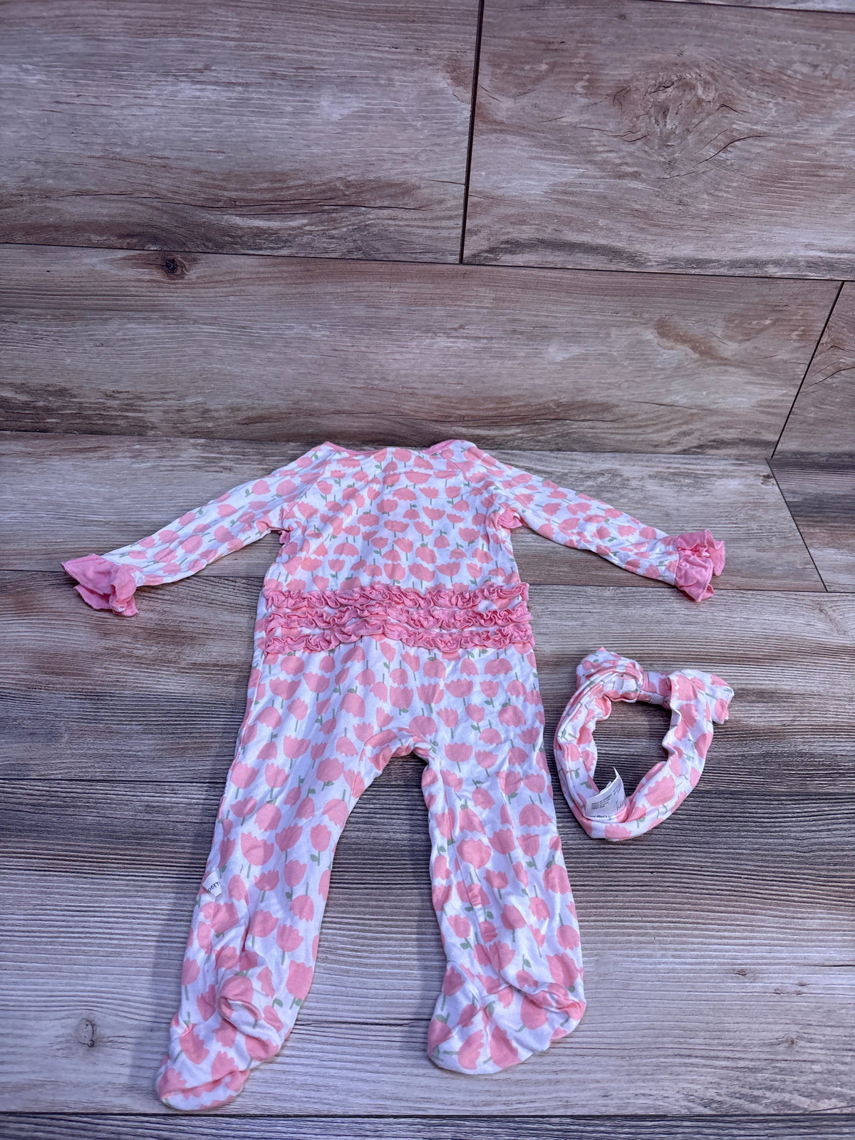 Overhead view of a two-piece baby footie and headband set showcasing pink floral print and ruffled details on a wood floor