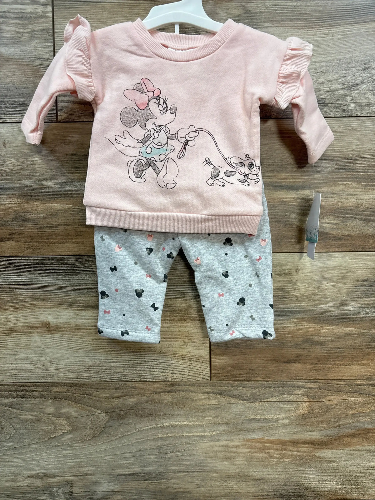 Pink baby outfit with Minnie Mouse holding a dog and gray pants with Mickey Mouse patterns on wood