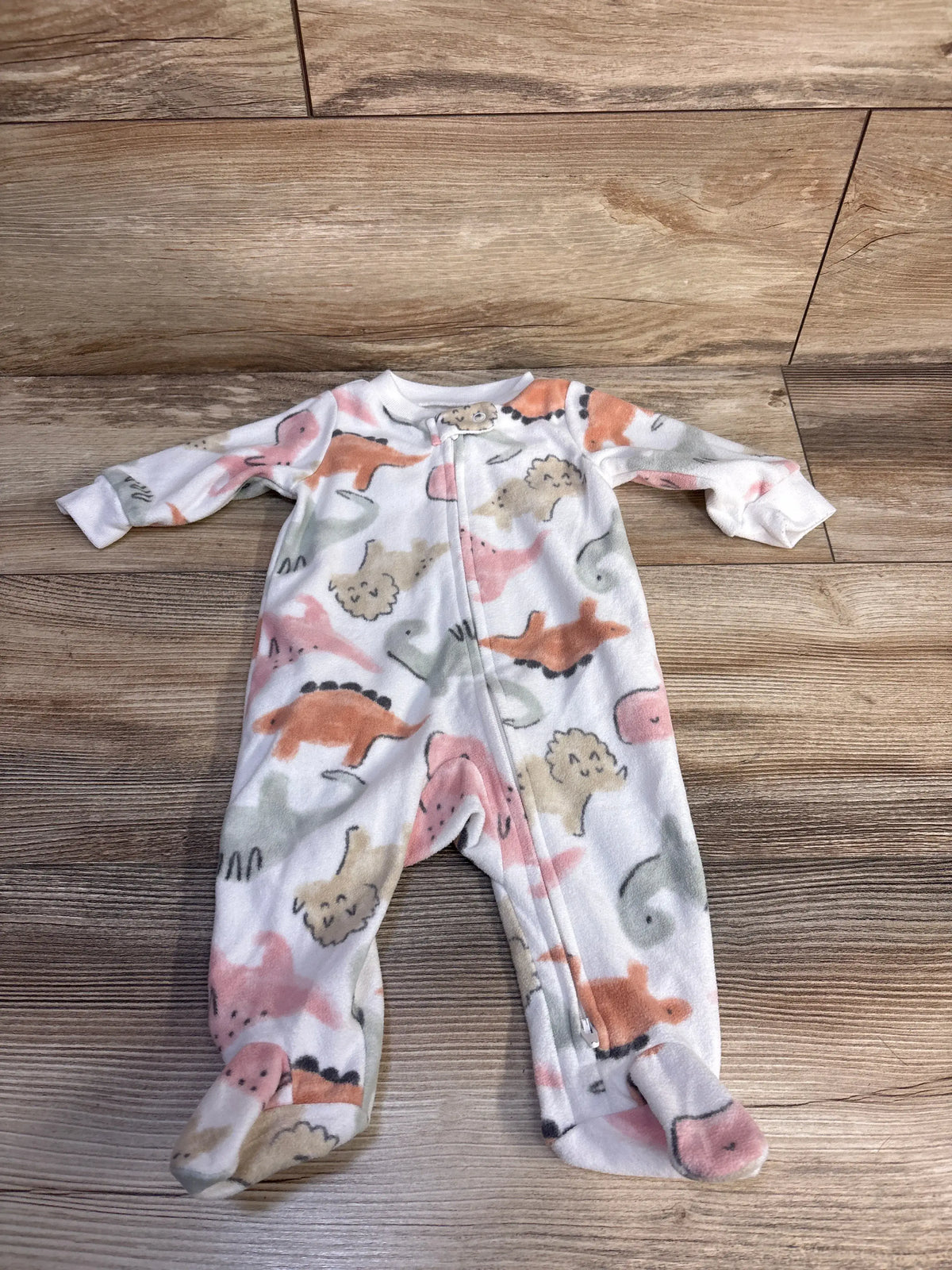 Front view of Carter’s white dinosaur blanket sleeper showcasing footed legs and colorful dinosaur print on a wood floor
