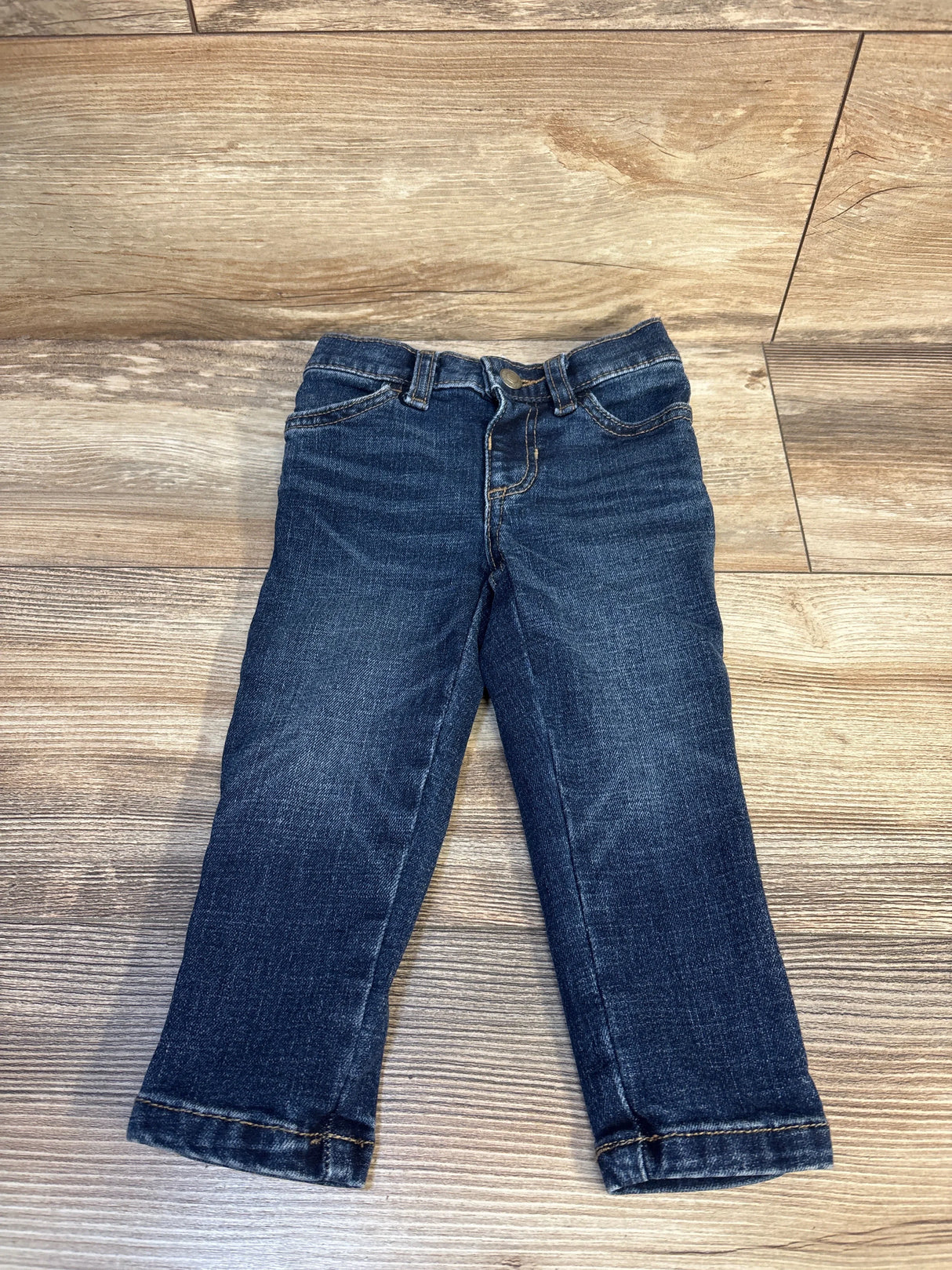 Dark wash denim jeans for toddlers displayed on wooden background