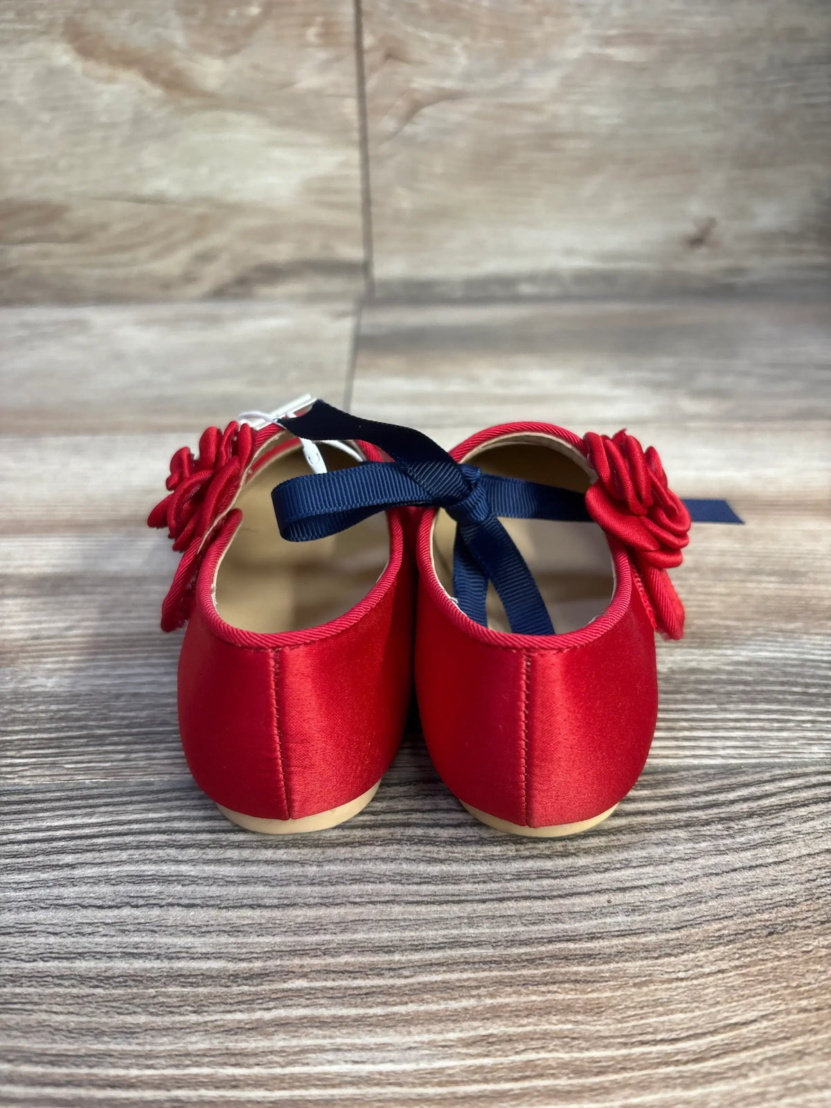Rear view of Janie and Jack red satin rosette ballet flats showcasing rosette detail and navy ribbon ties on wood floor background