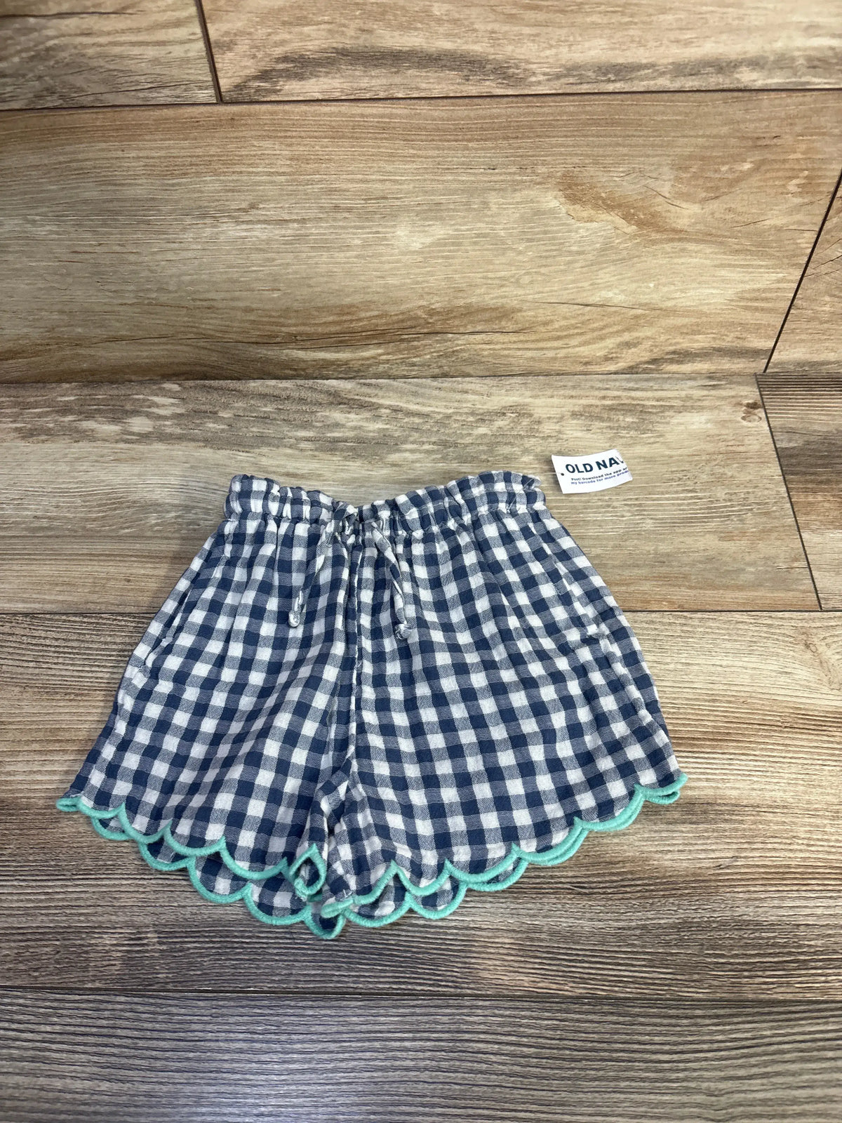Front view of blue and white checkered gauze shorts with elastic waistband, drawstring, and turquoise scalloped trim
