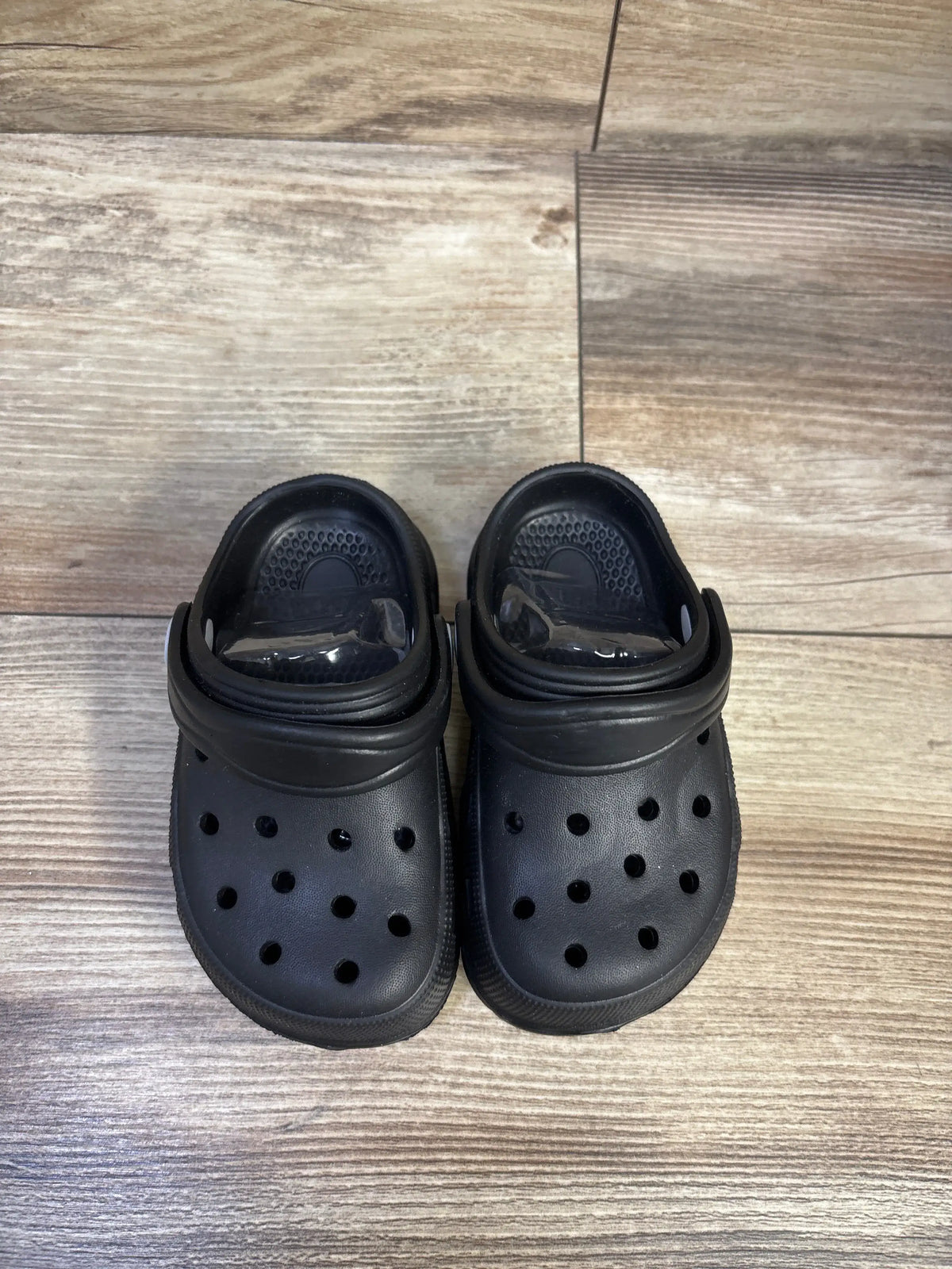 Top view of Hobibear toddler black clogs showcasing ventilation holes and adjustable heel straps on wood floor, size 5C