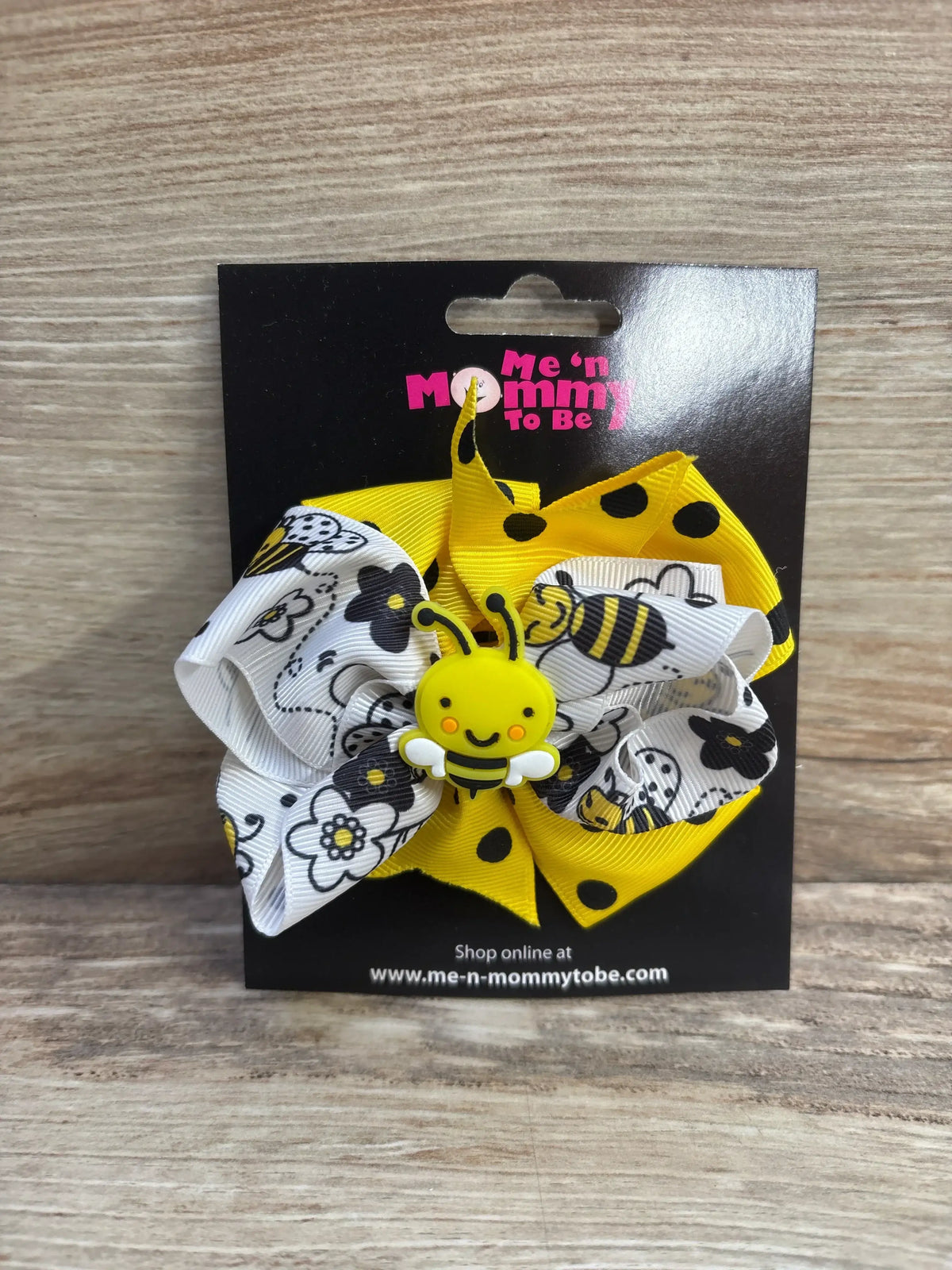 Front view of yellow and white bee bow with smiling bee applique and polka-dot and floral ribbons on black card over wood